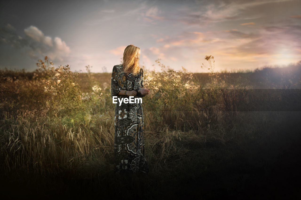 Young woman standing on grassy field against sky during sunset