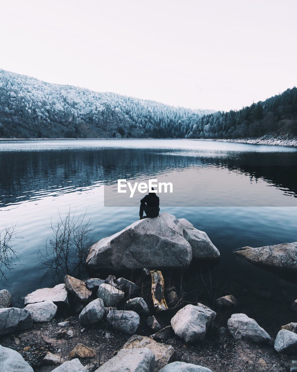 Man relaxing by lake against sky