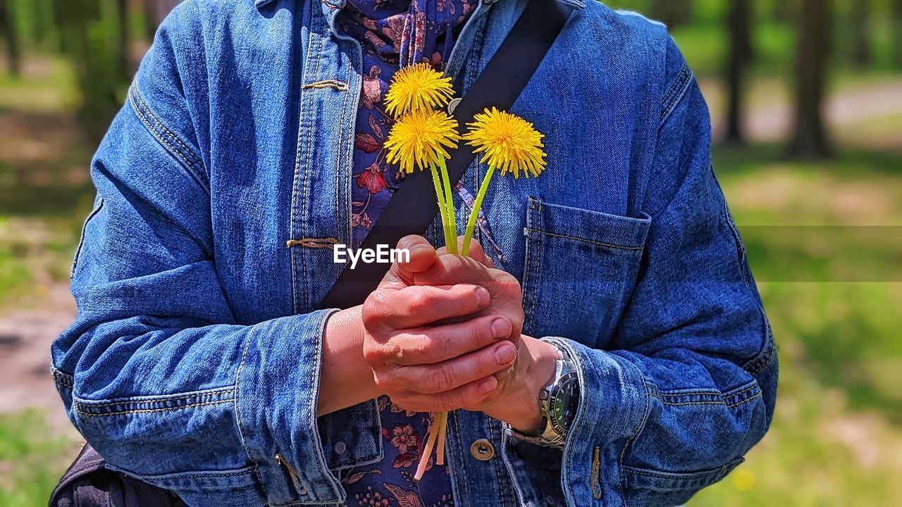 flower, flowering plant, plant, nature, adult, holding, one person, hand, fragility, yellow, beauty in nature, midsection, men, casual clothing, outdoors, freshness, focus on foreground, lifestyles, day, emotion, person, women, blue, front view, spring, growth, leisure activity, clothing, close-up, standing, rural scene