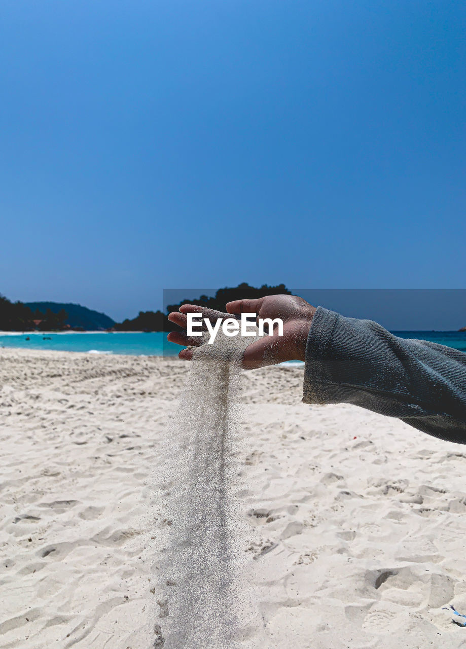 Man throwing sand on beach against clear sky