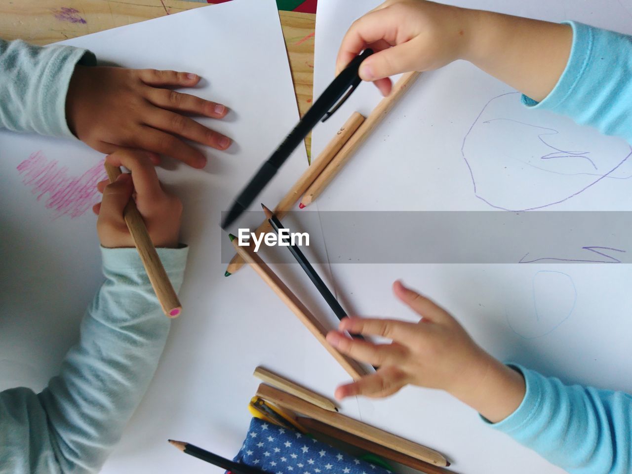 Cropped hands of children drawing on cardboard