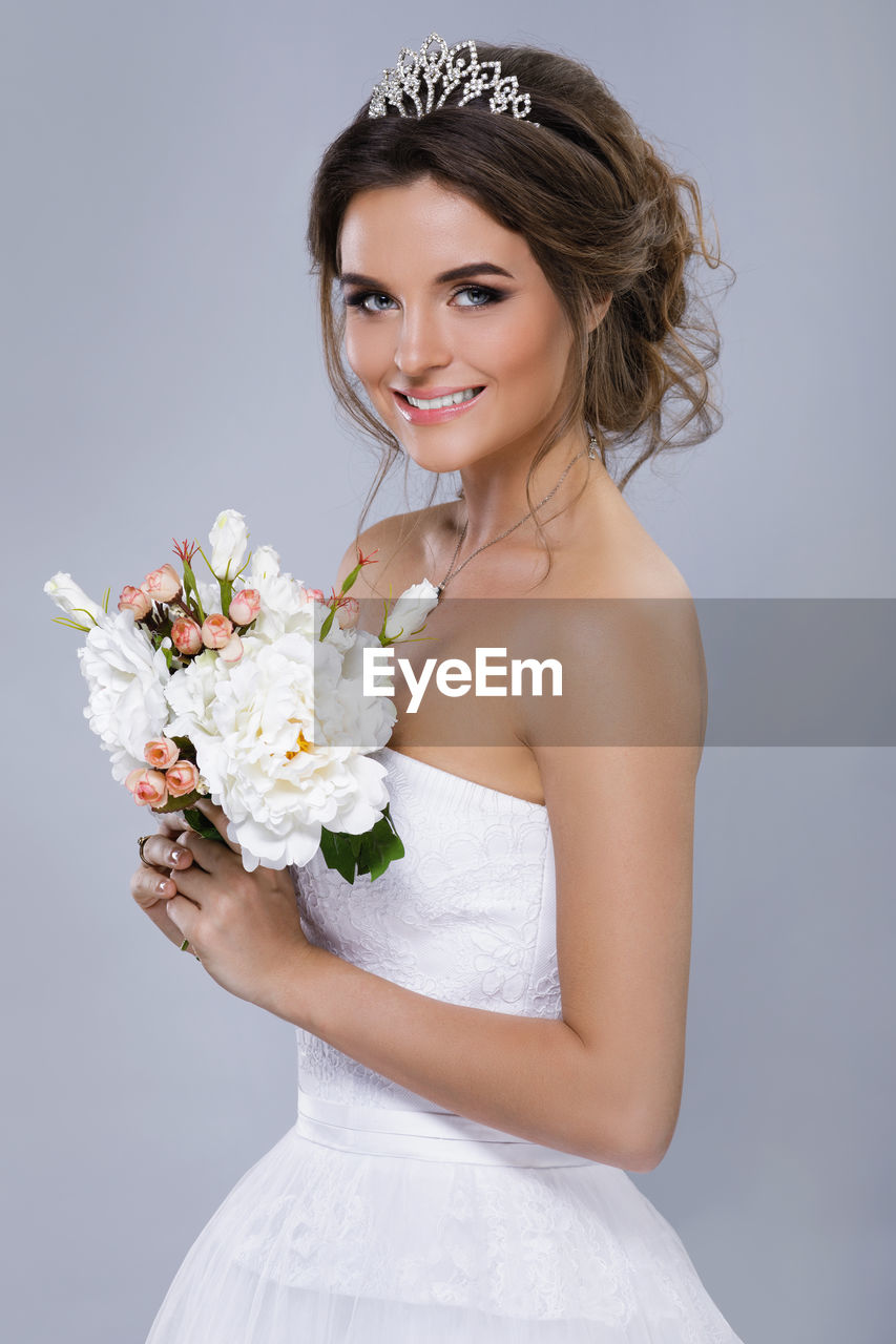 Side view of bride holding bouquet against gray background