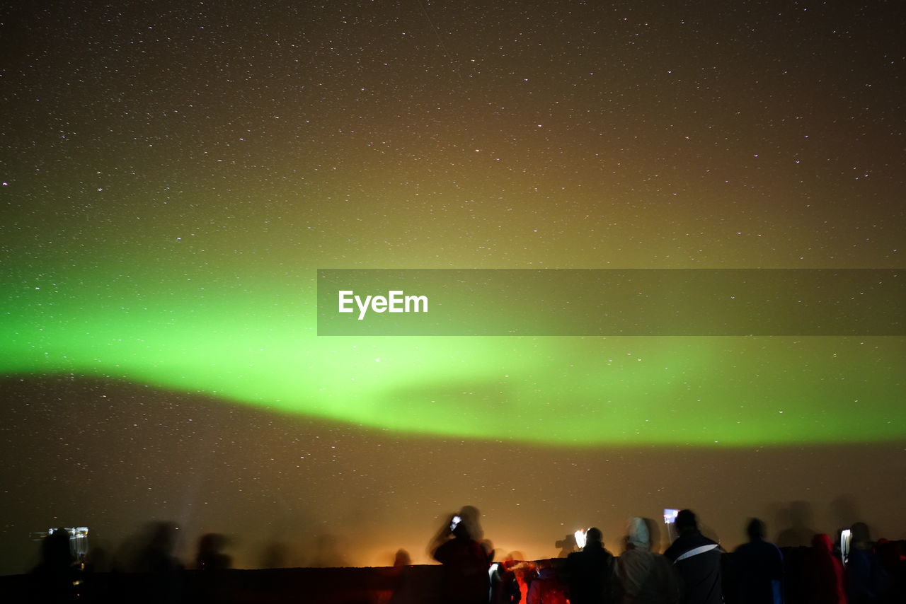 Blurred motion of people with aurora borealis in sky at night