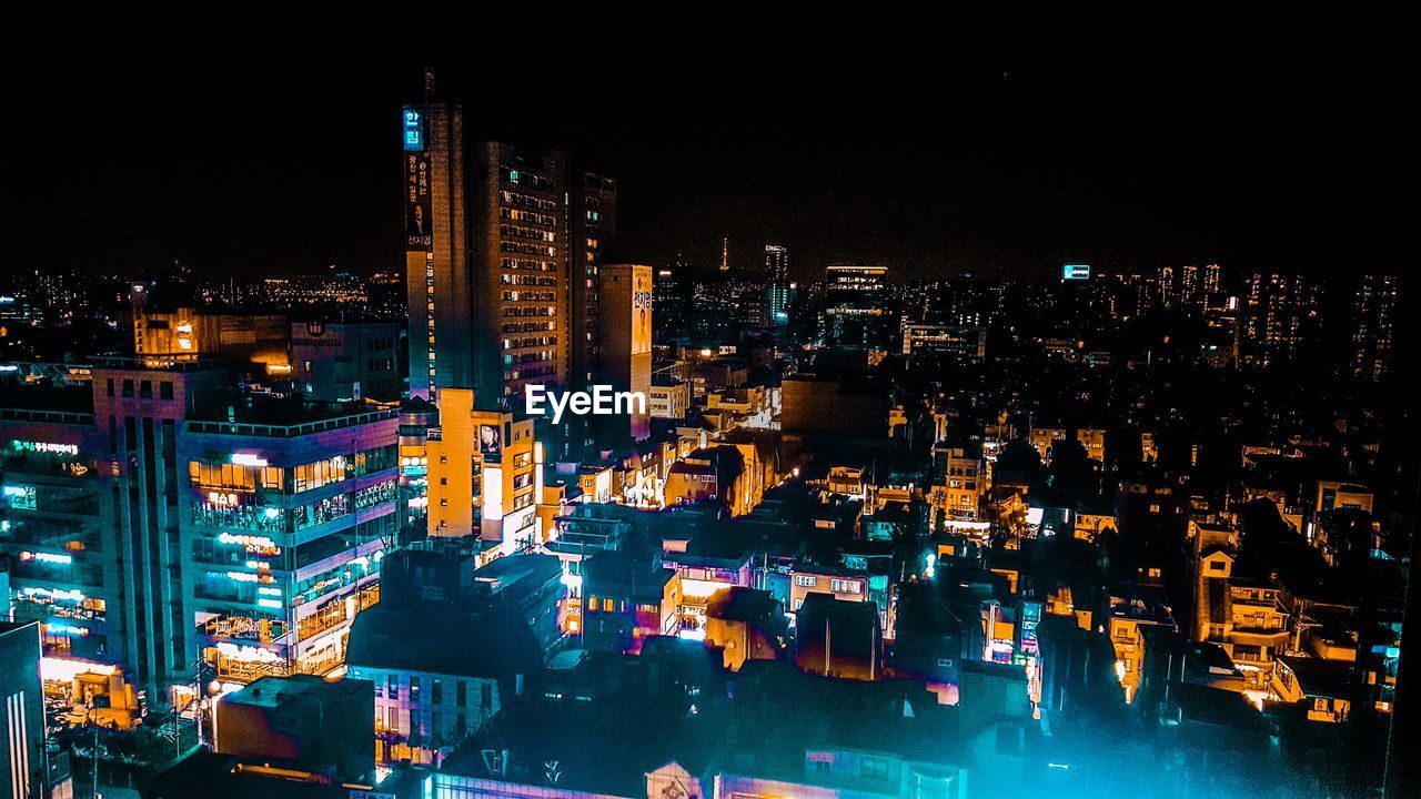 HIGH ANGLE VIEW OF ILLUMINATED BUILDINGS AGAINST SKY AT NIGHT