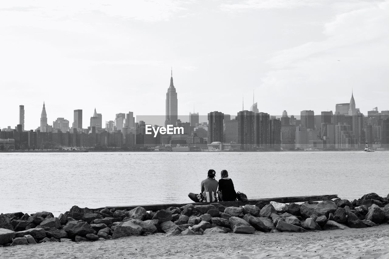 Rear view of man and woman sitting on retaining wall in front of hudson river