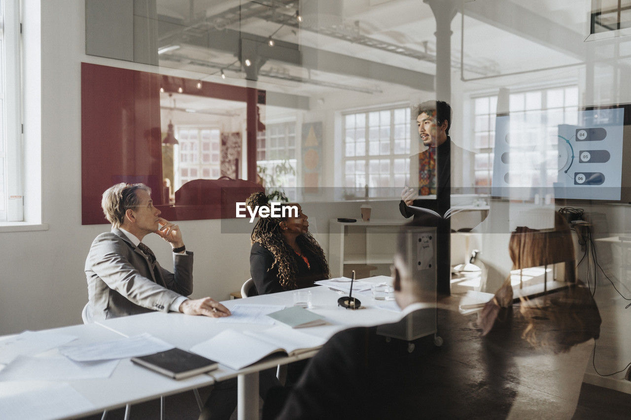 Business colleagues conducting meeting in board room at office seen through glass