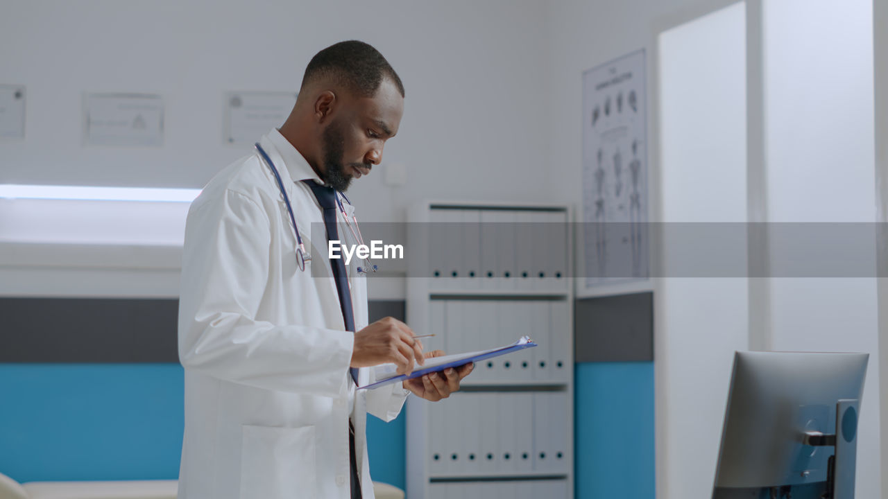 Side view of doctor looking at clipboard in clinic