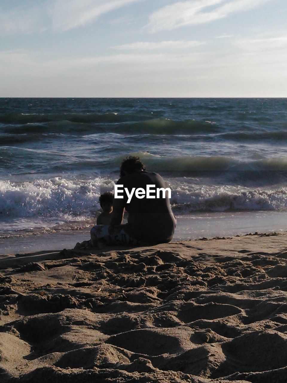 REAR VIEW OF MAN SITTING AT BEACH