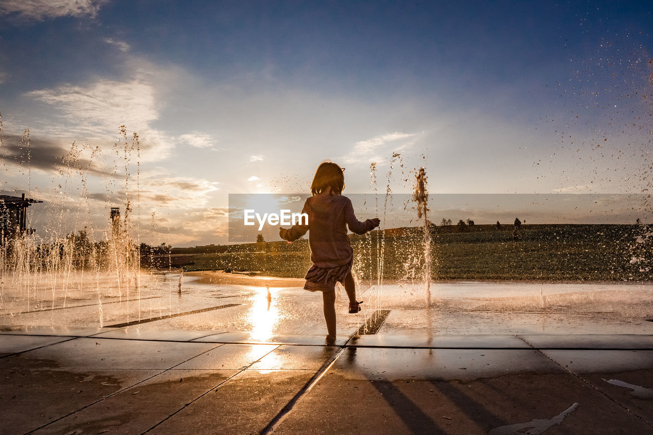 Young girl hold her foot in the water at a splash pad at sunset