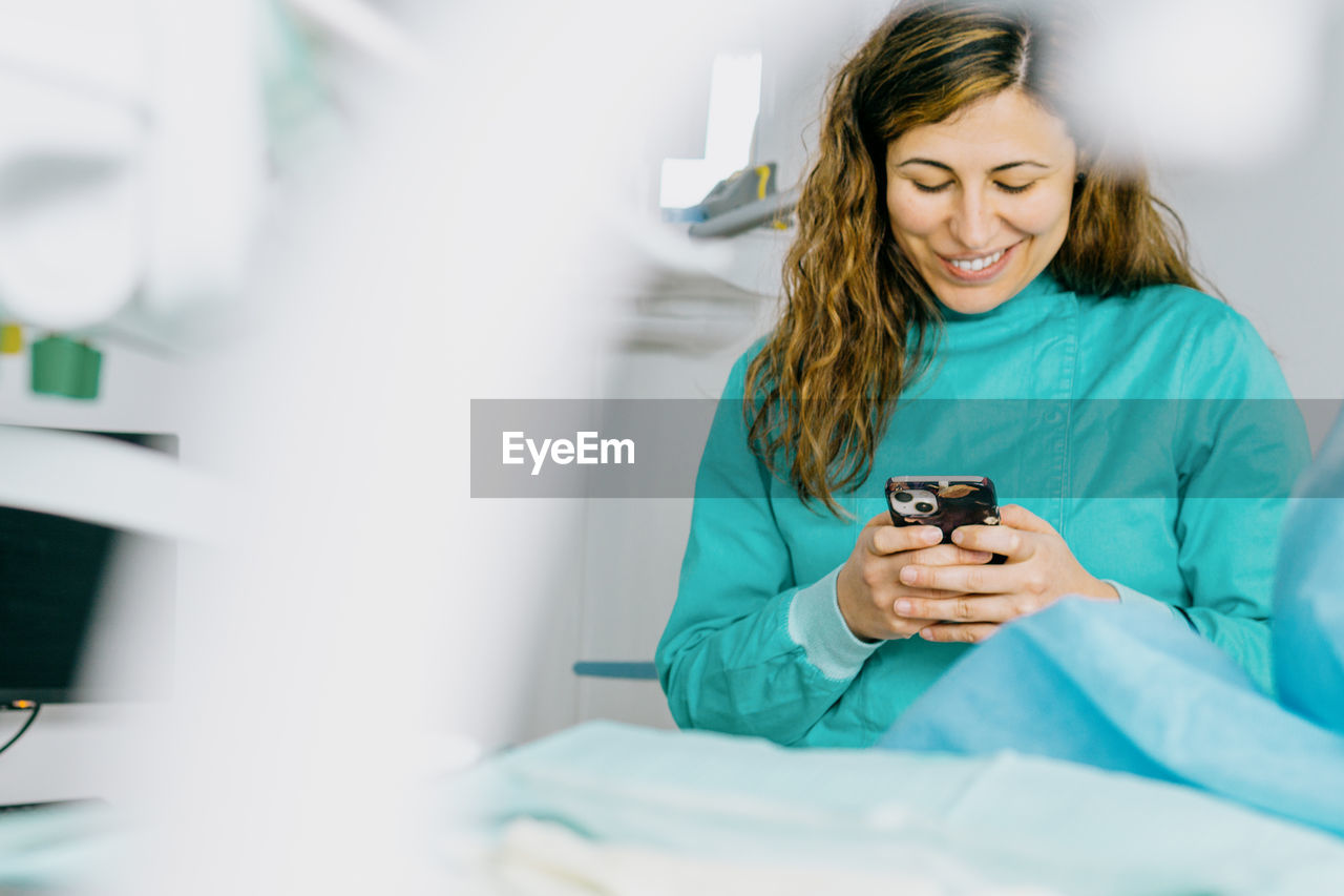 adult, women, blue, healthcare and medicine, indoors, technology, occupation, female, smiling, one person, person, doctor, bed, hospital, furniture, professional occupation, patient, happiness, communication, holding, expertise, looking, lifestyles, young adult, sitting, working, clothing, wireless technology, emotion, care