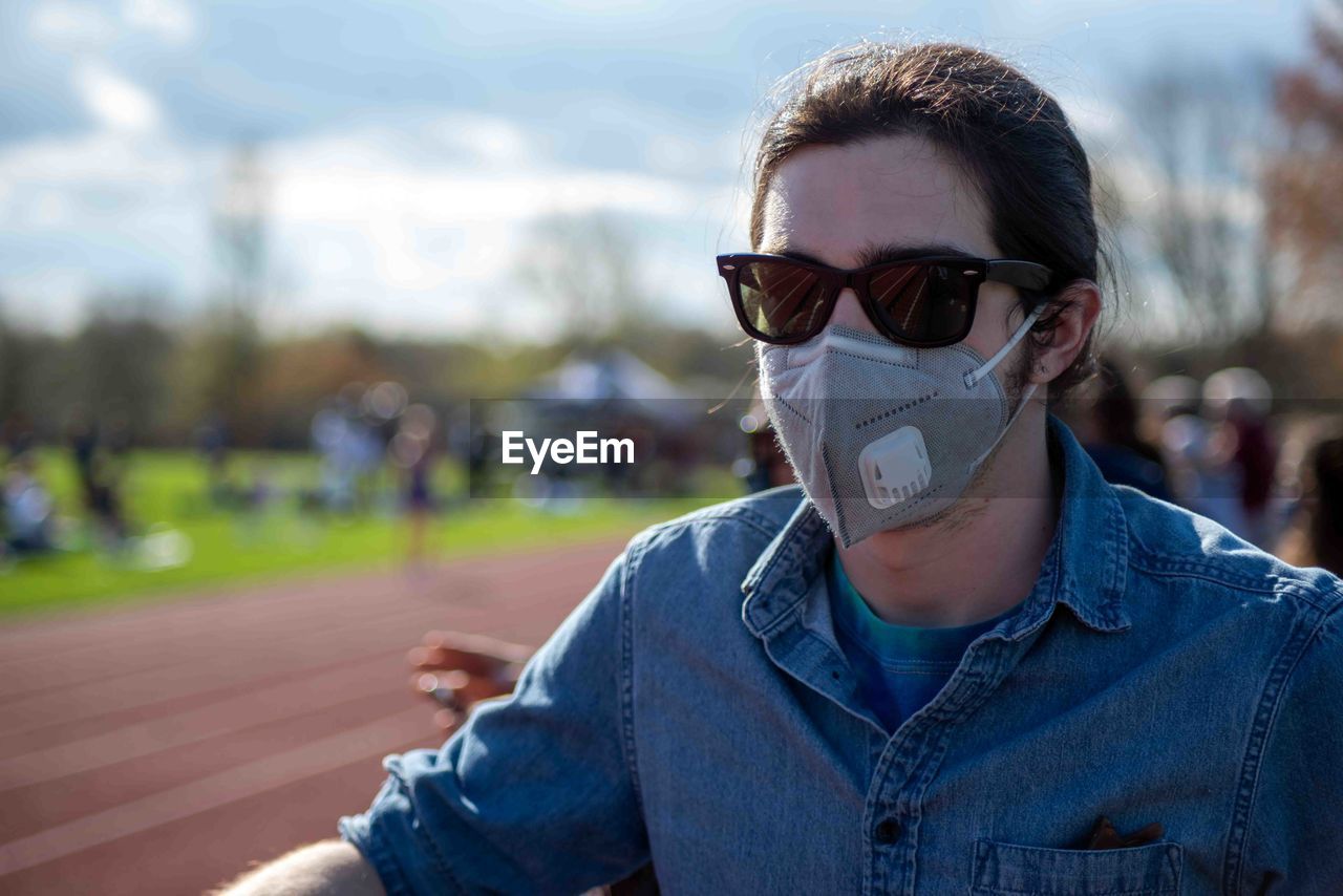 Young man with face mask stands by athletic track