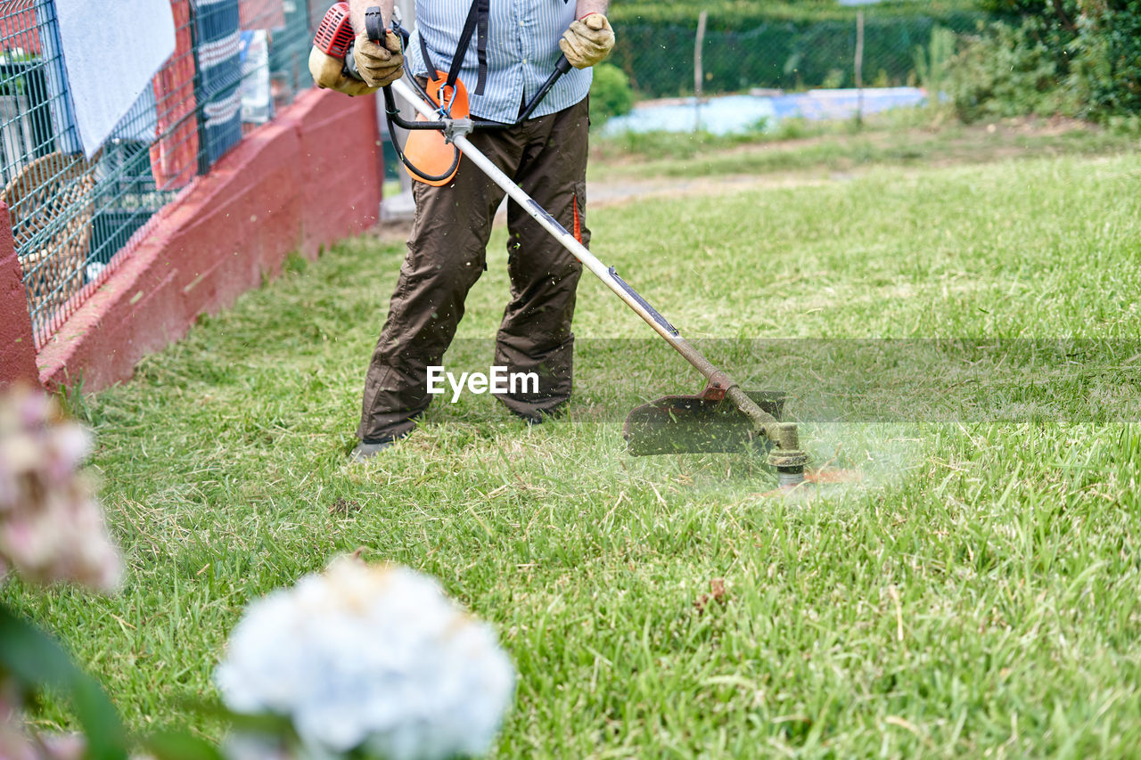 Crop elderly man mowing grass in backyard with lawn mower