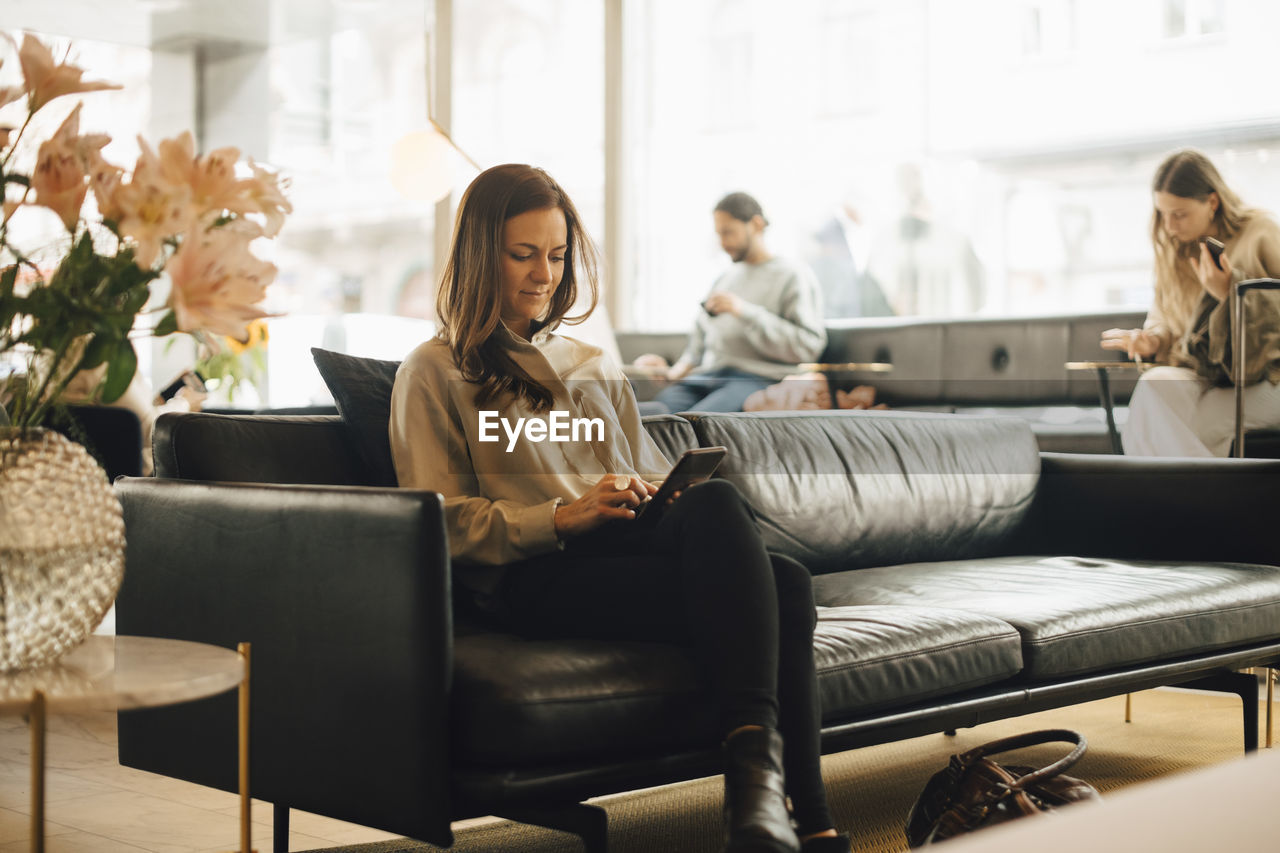 Full length of woman using smart phone while sitting on sofa in restaurant