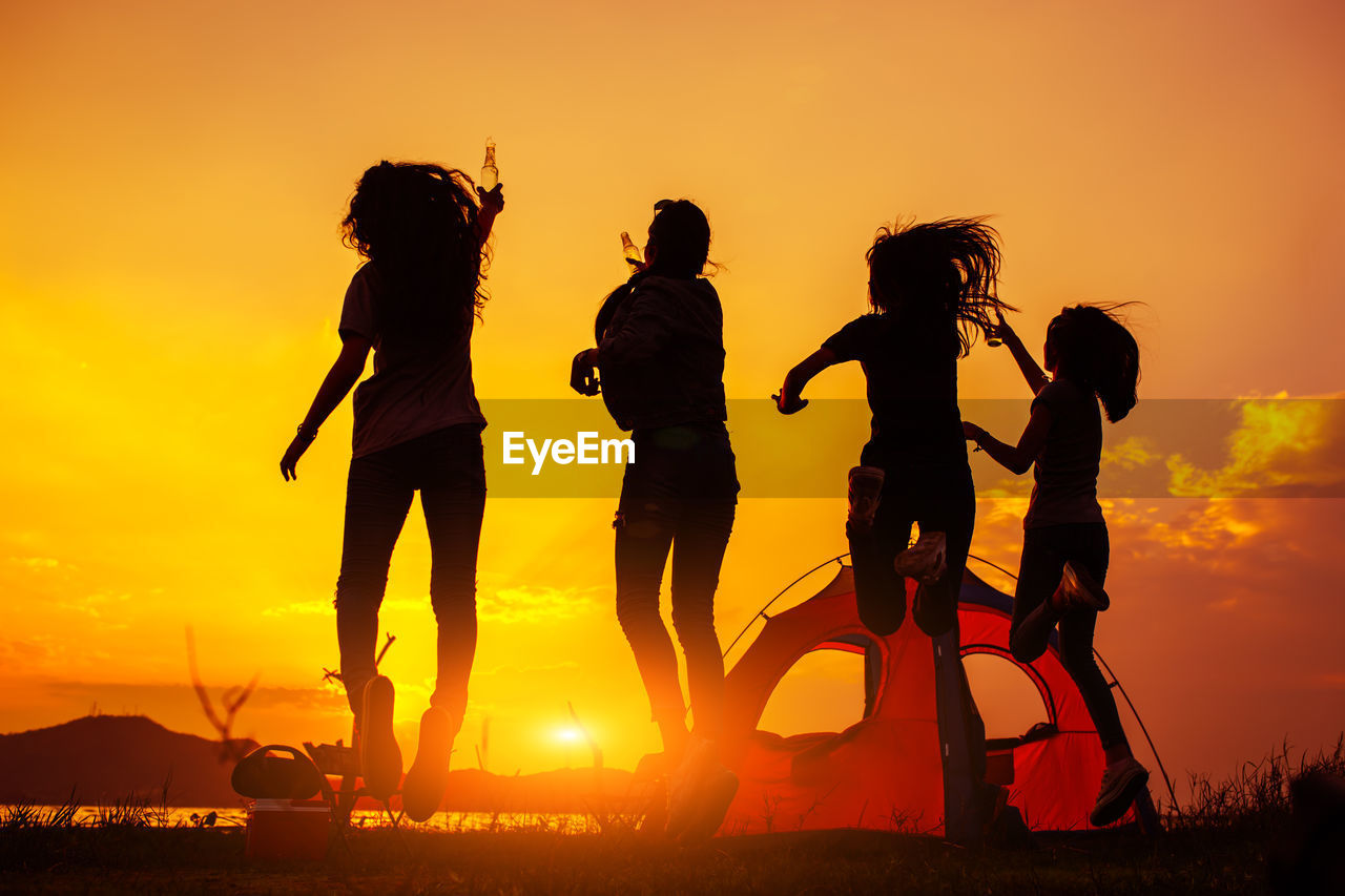 Happy friends enjoying camping at beach during sunset