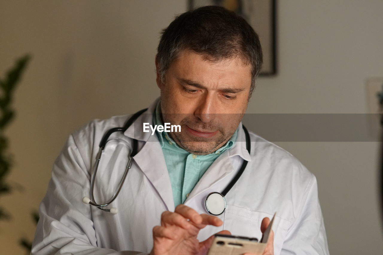 Close-up of mature doctor using phone against wall
