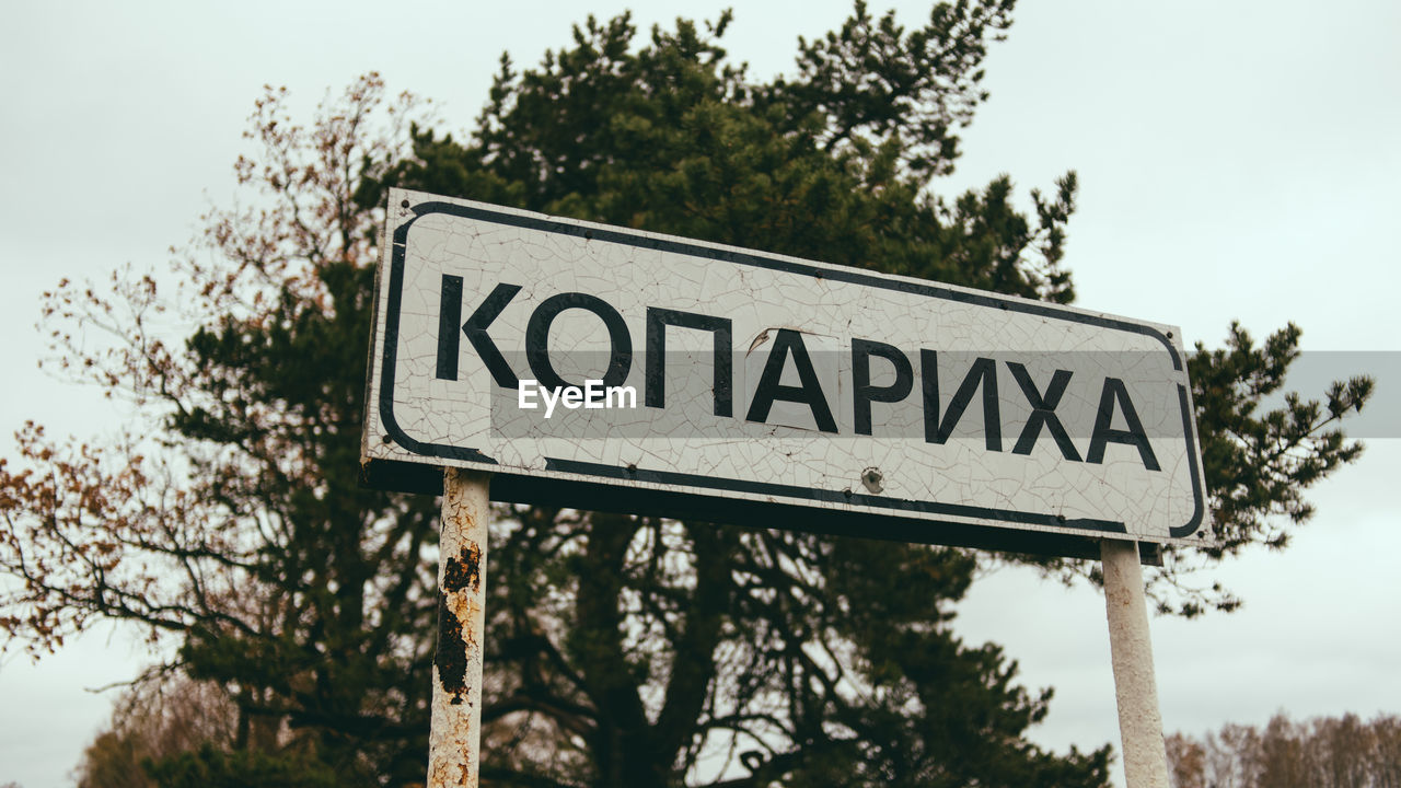 Low angle view of information sign against tree and sky