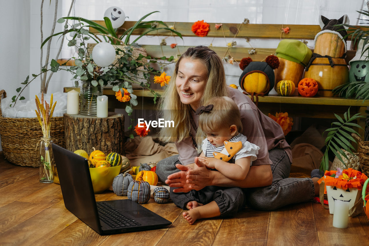 Mother with daughter clapping while sitting in front of laptop on floor at home