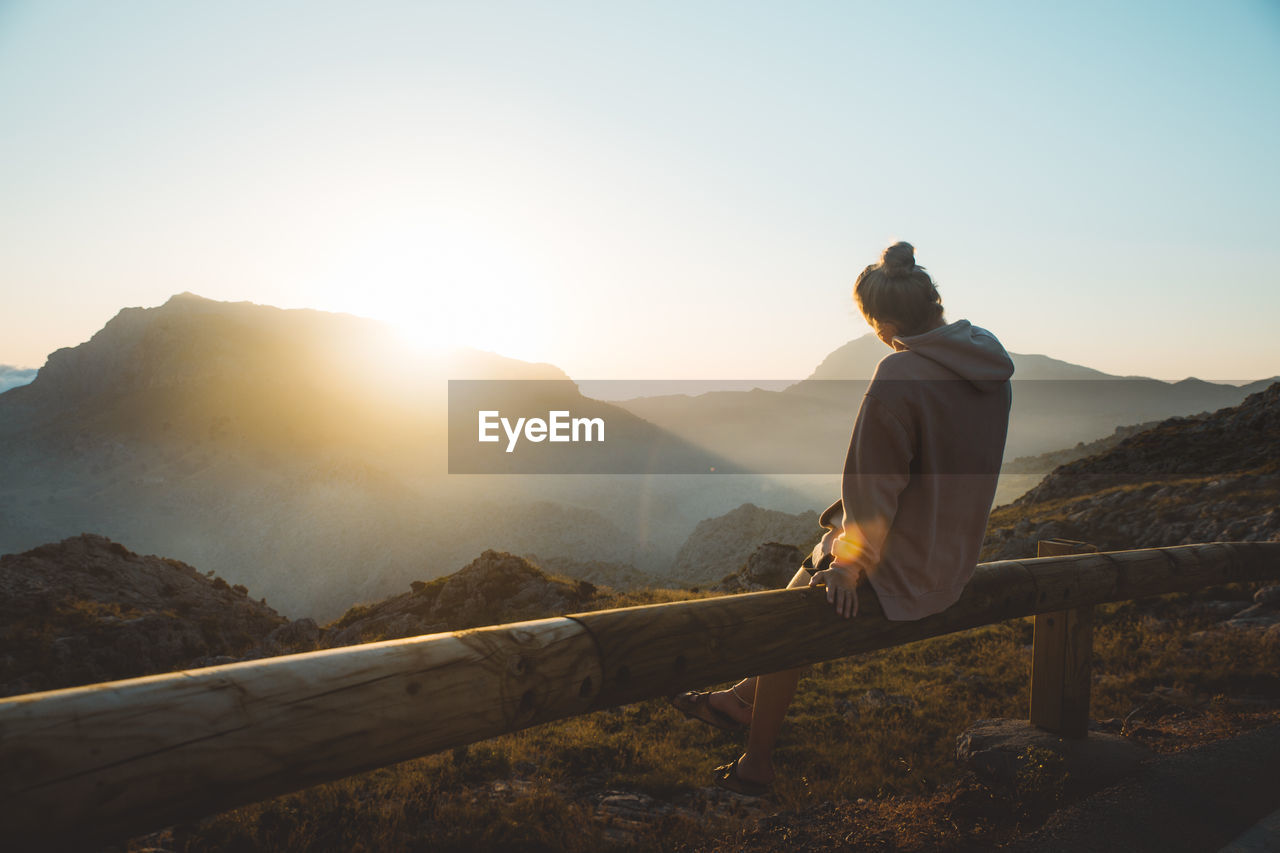 Rear view of young woman looking at mountains while sitting on railing