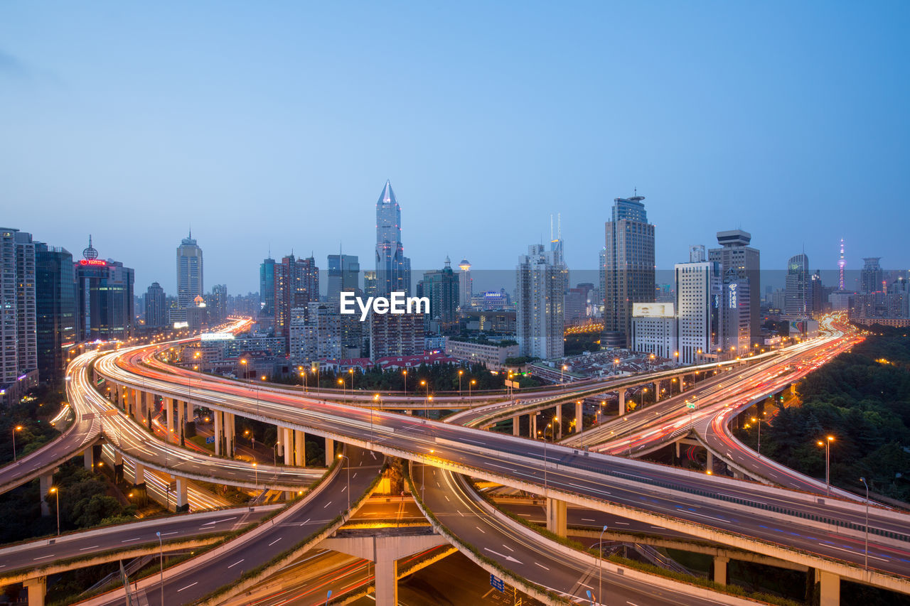 High angle view of light trails on road amidst buildings in city against sky