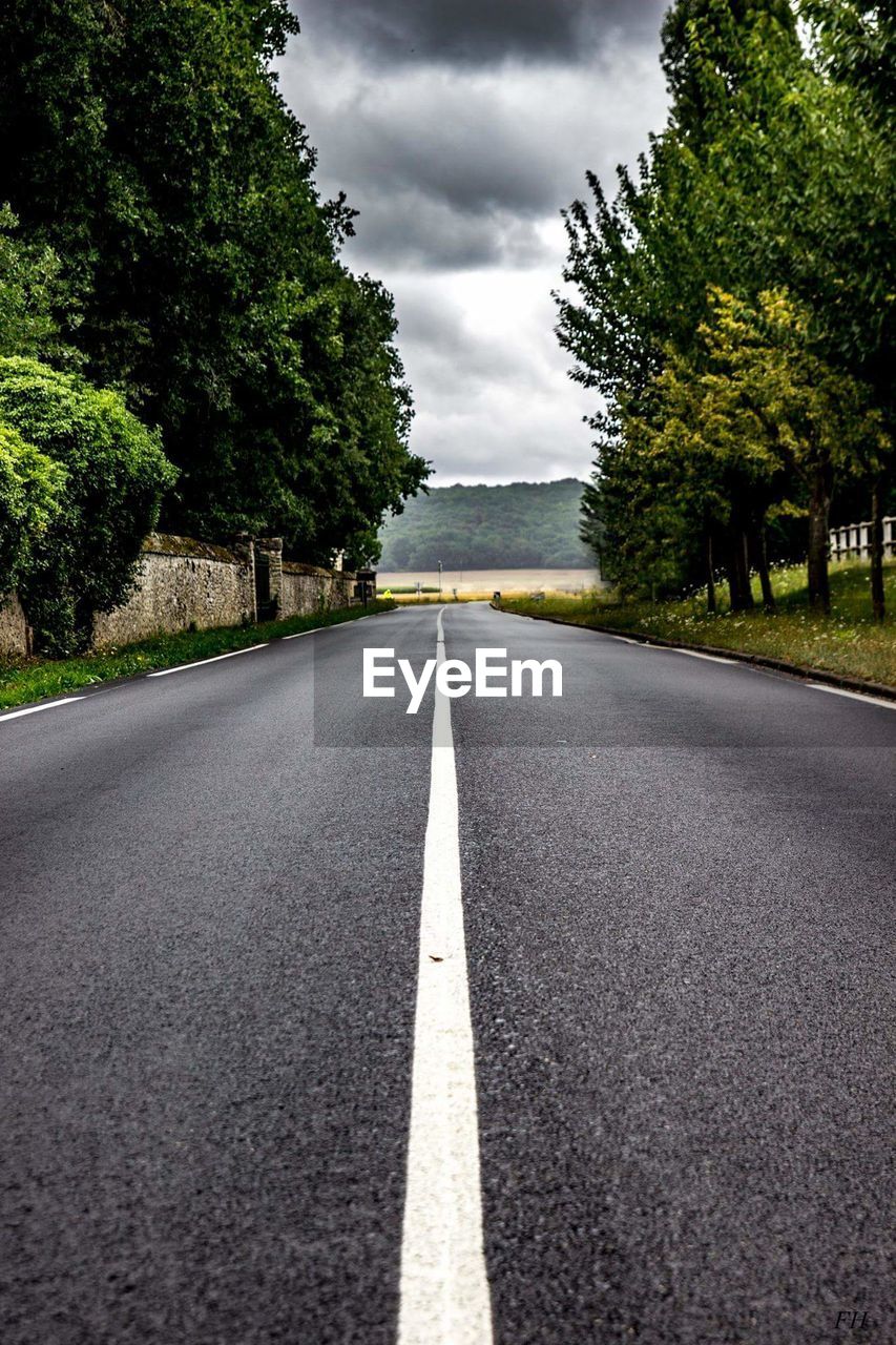 Empty road amidst trees against sky