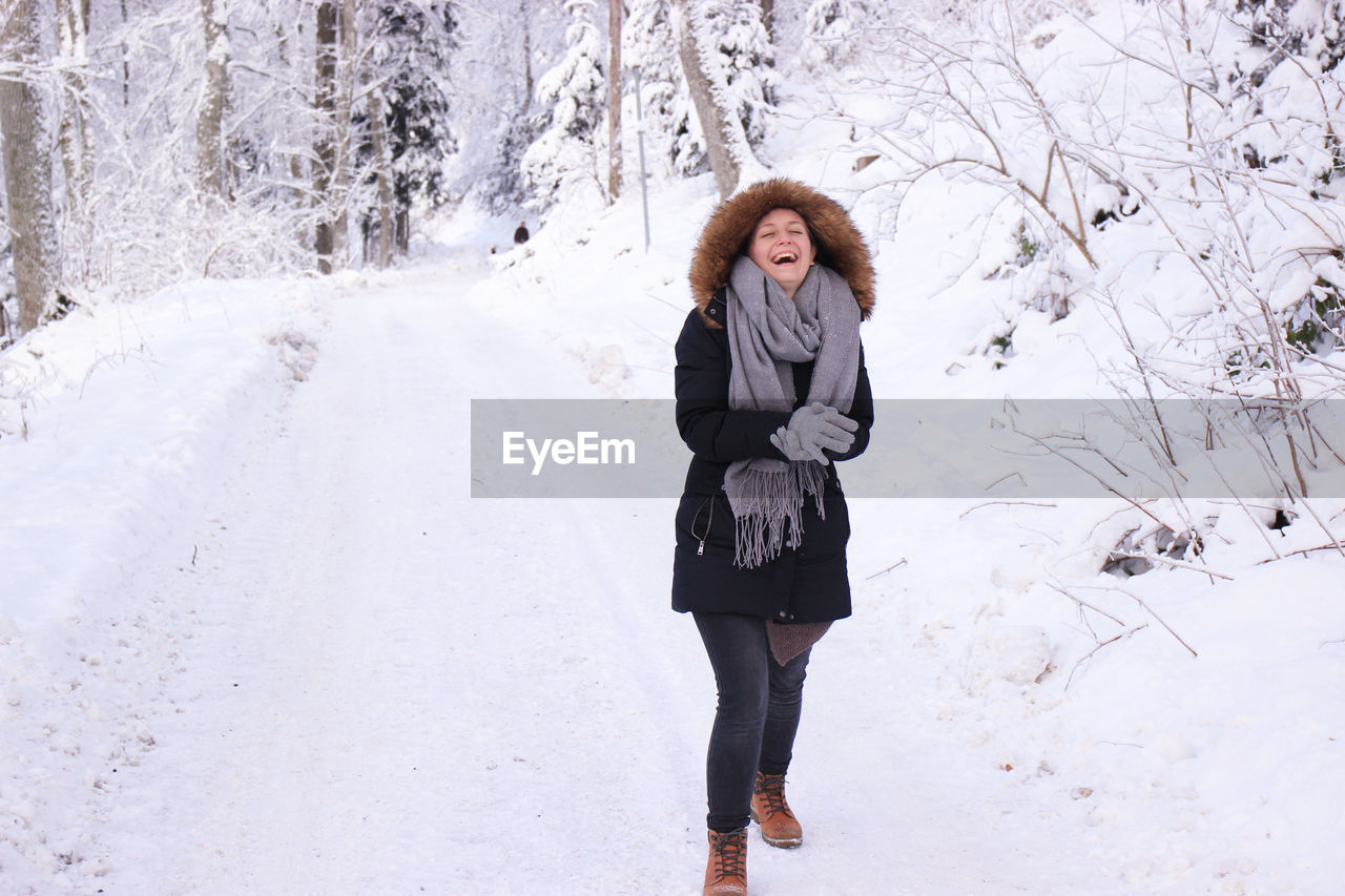 Cheerful young woman wearing warm clothing standing in snow