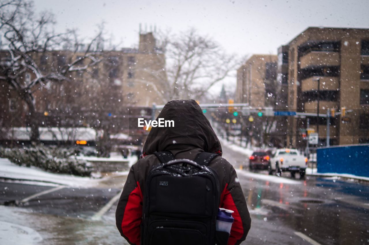 Rear view of man walking on city street during snowfall
