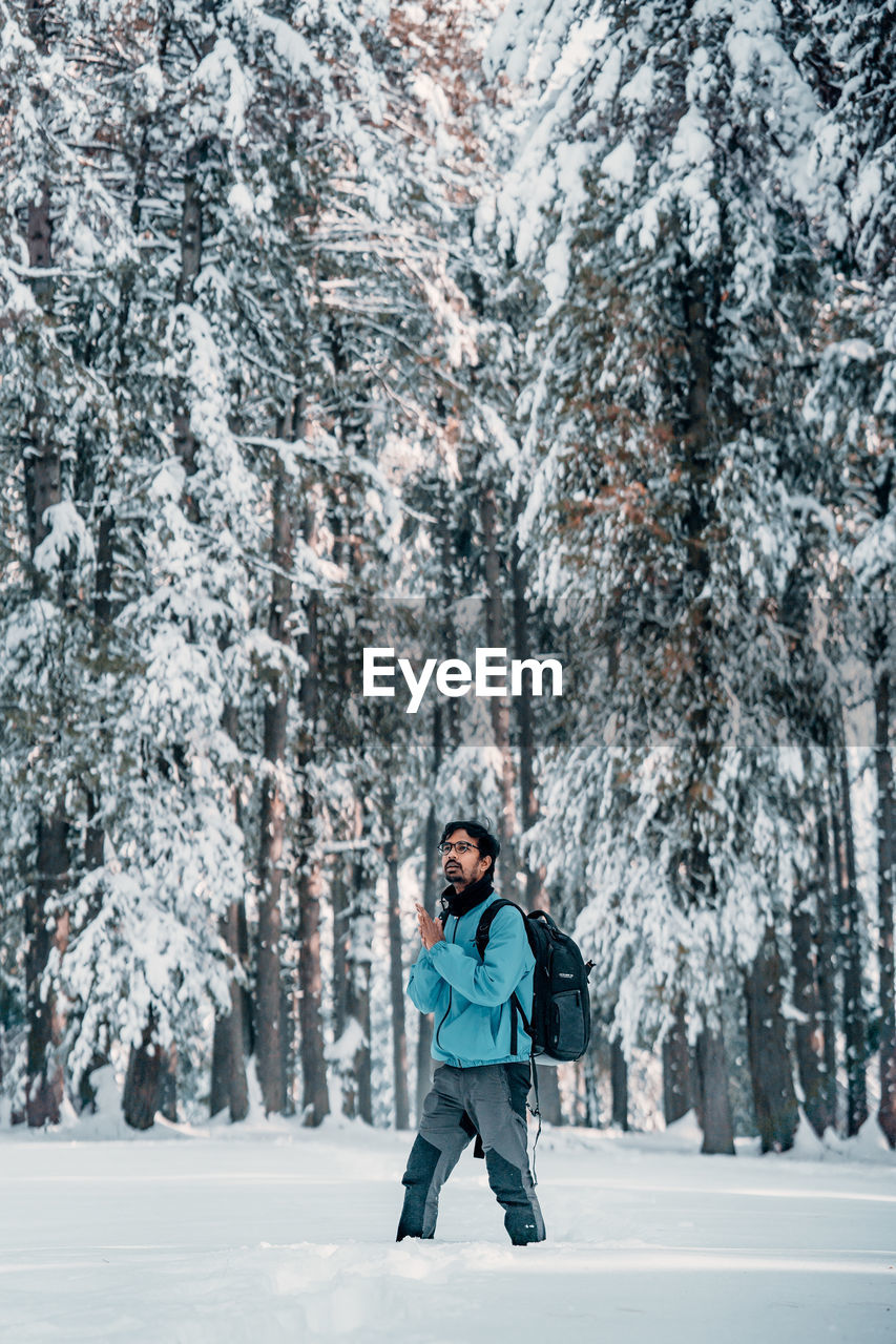 Young man walking on snow covered land against trees