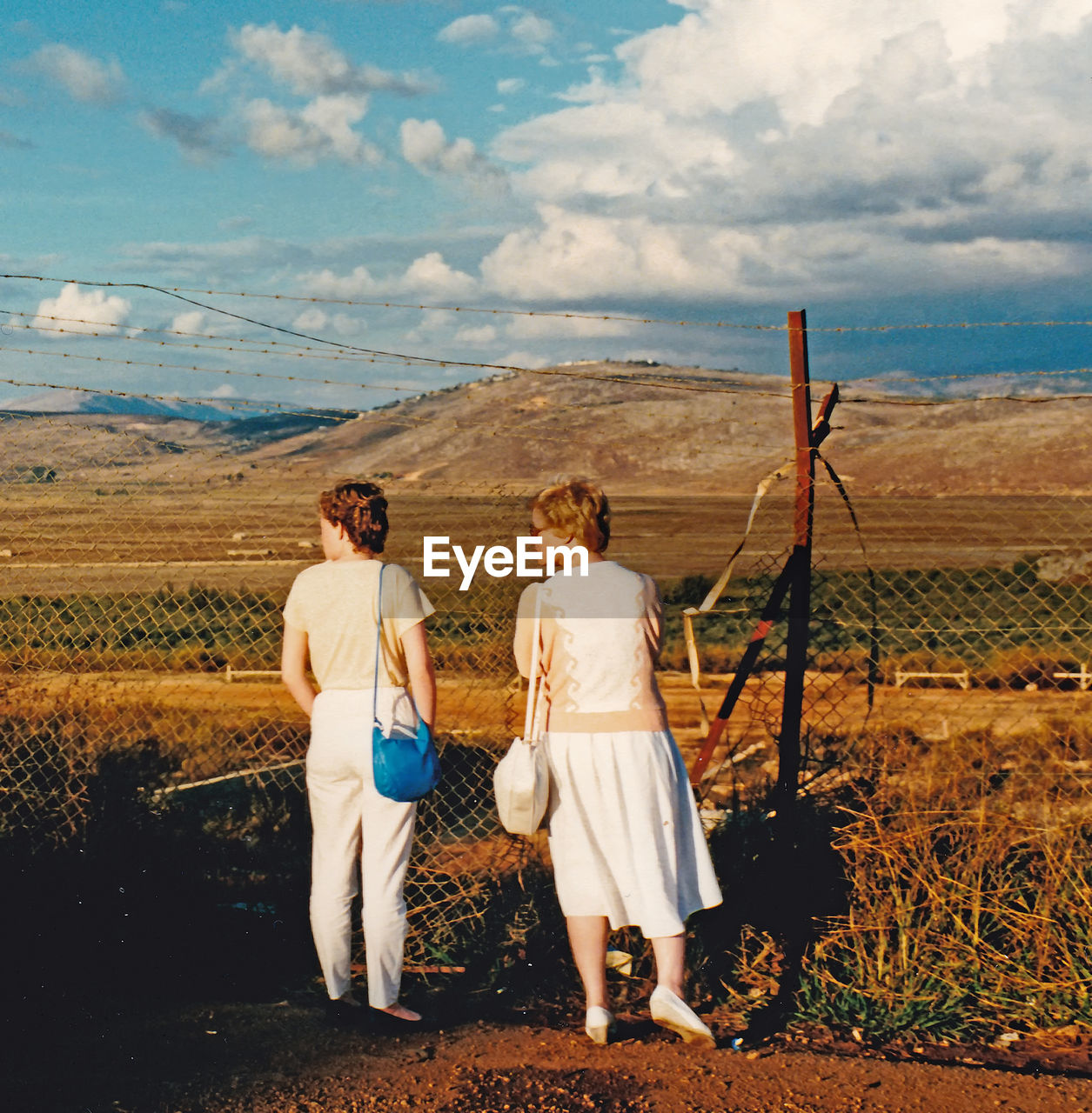 REAR VIEW OF COUPLE STANDING ON FIELD