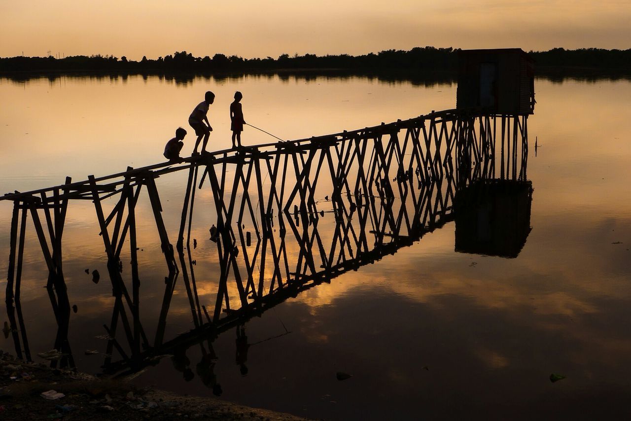 Silhouette children on pier over lake against sky during sunset