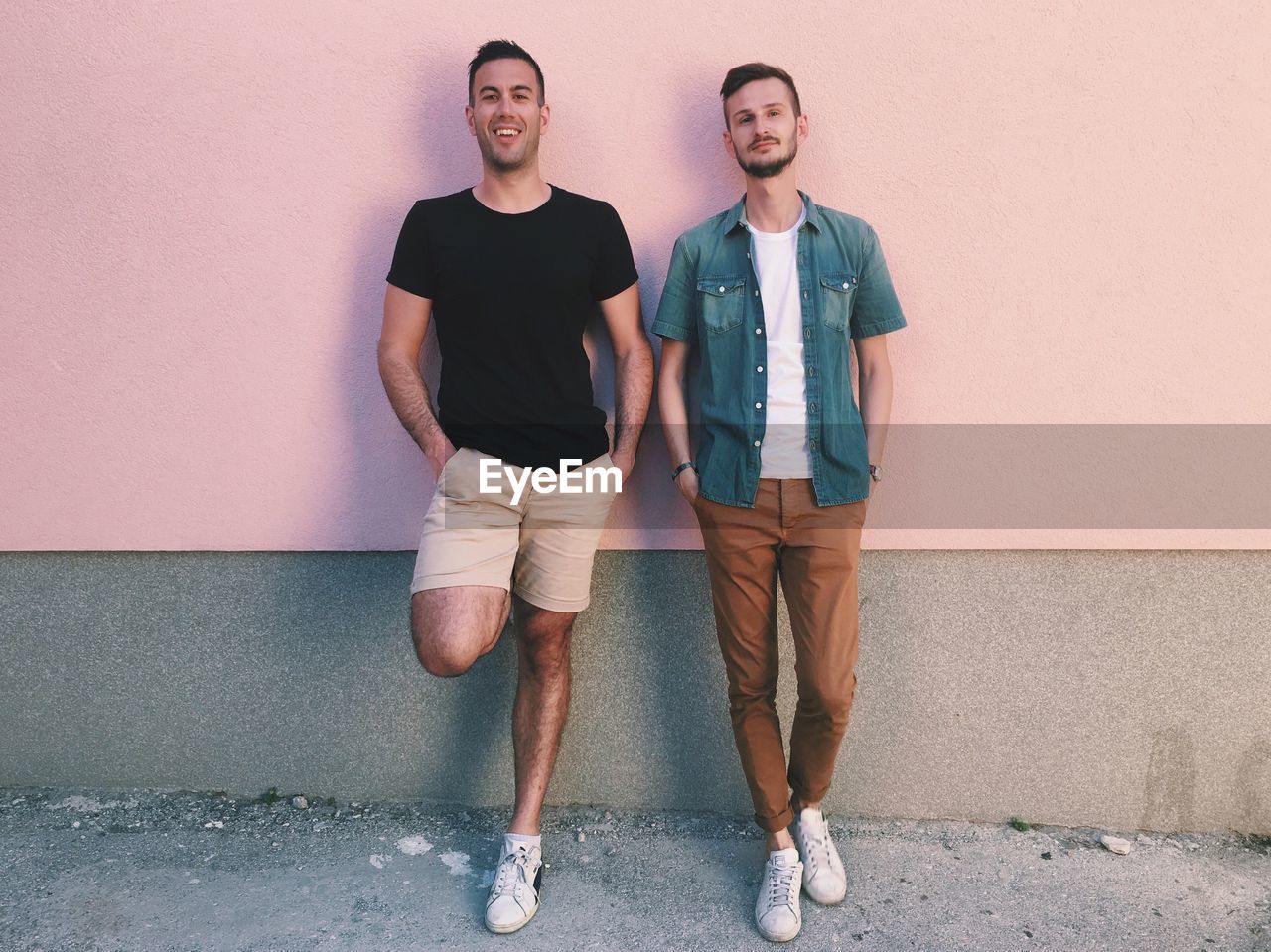 Full length of two men leaning on exterior wall