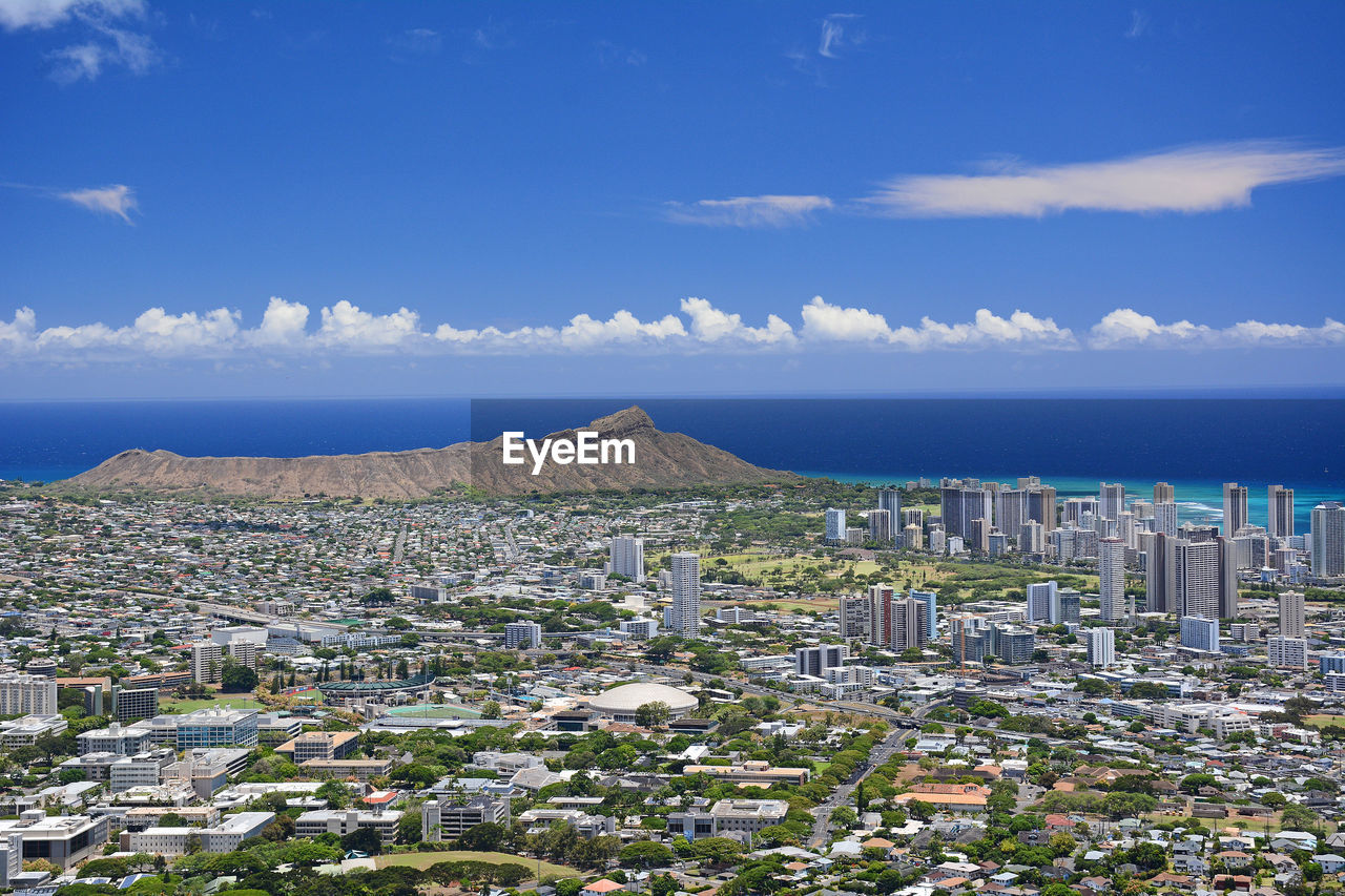 High angle view overlooking honolulu buildings against blue sky with diamond head in background. 