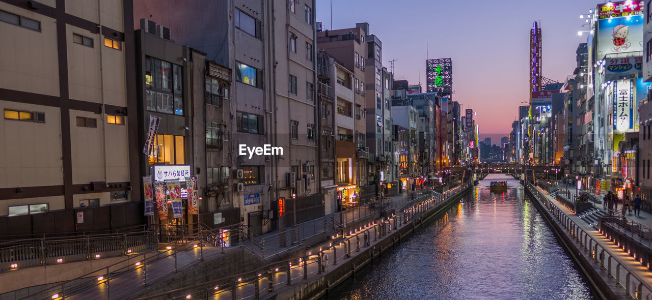 Canal amidst illuminated buildings in city during sunset