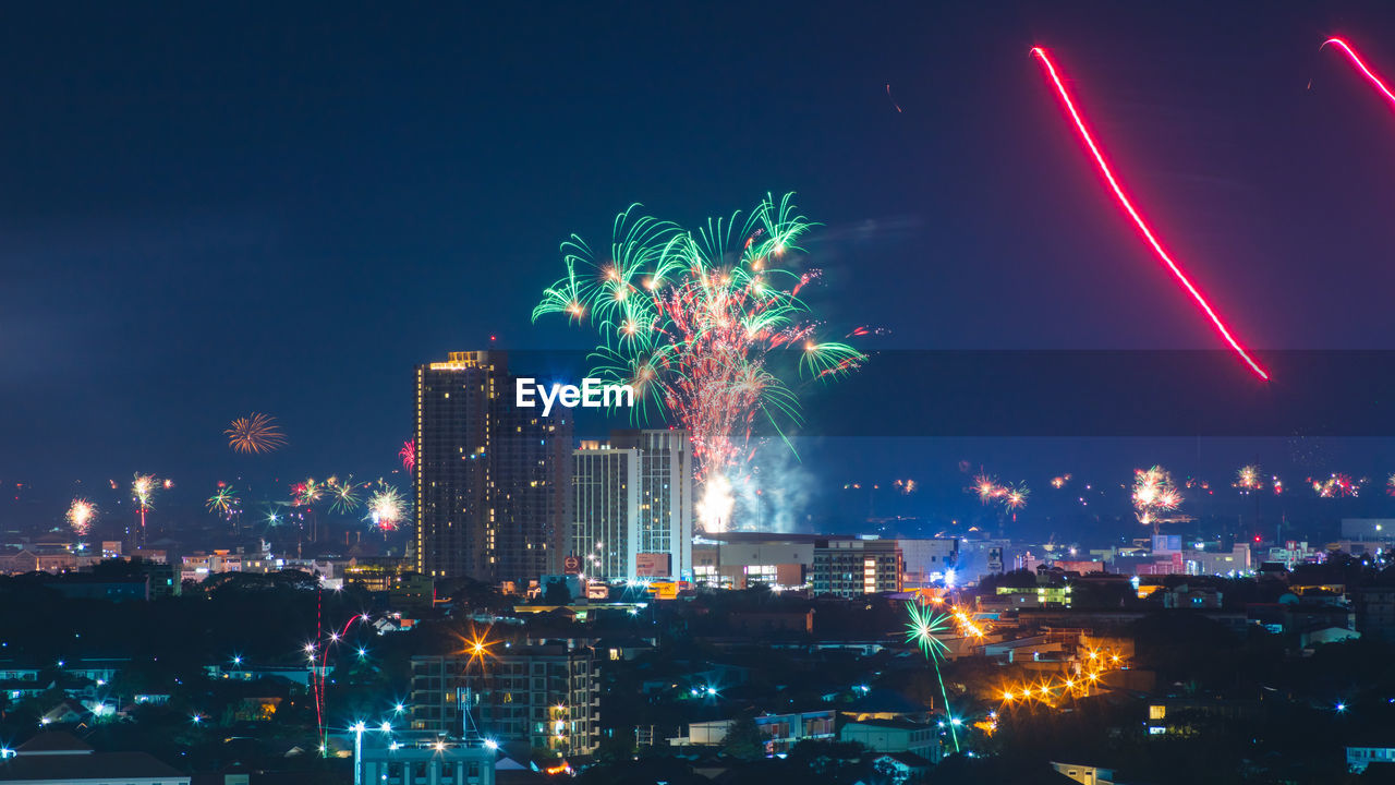 Firework display in city against sky at night