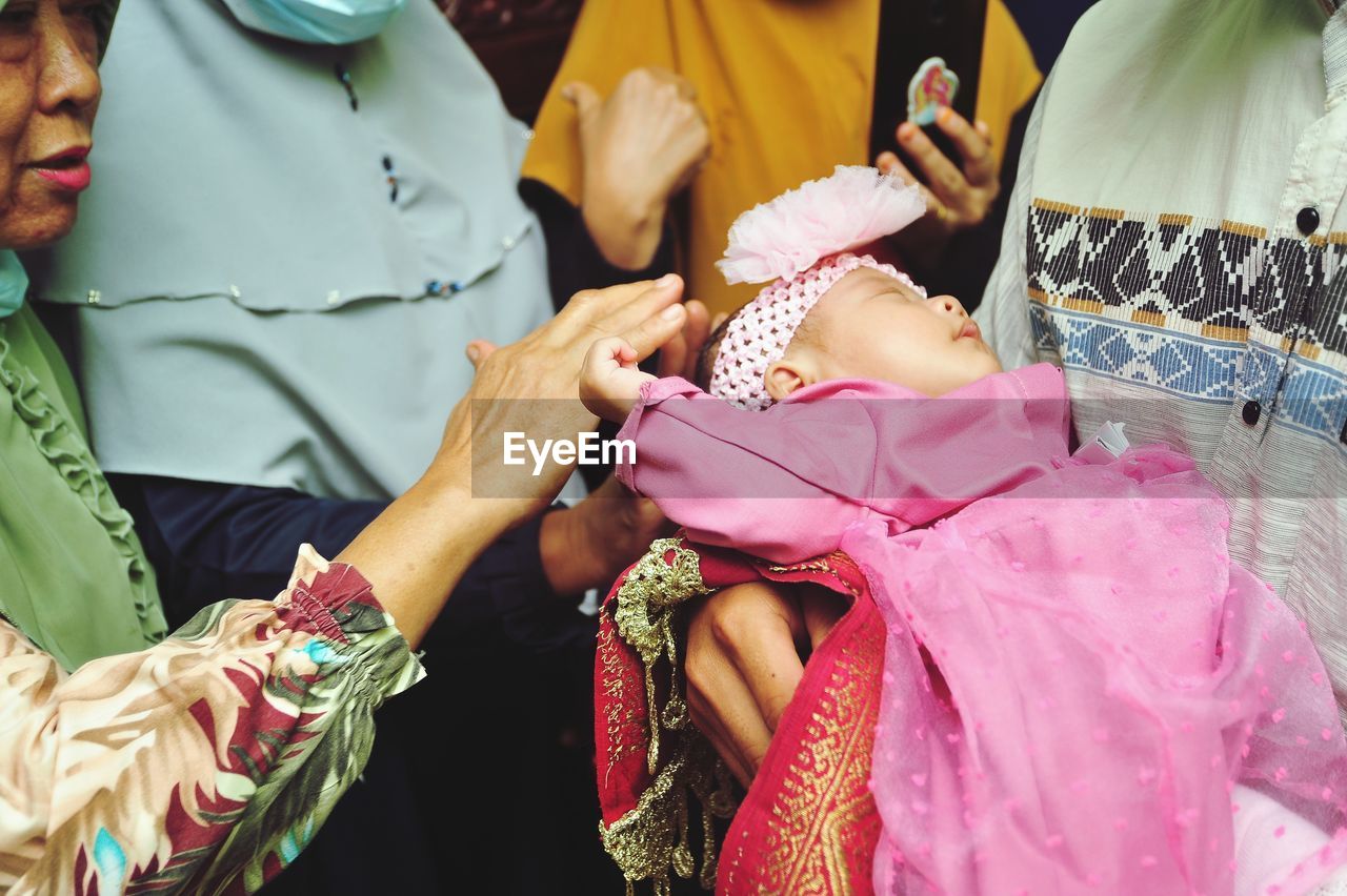 A child is caressed by his grandmother while sleeping on his father's lap on aqiqah event