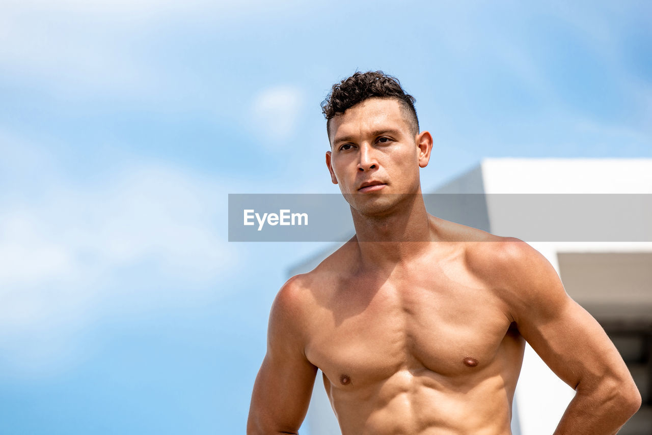 Young shirtless man standing against sky outdoors