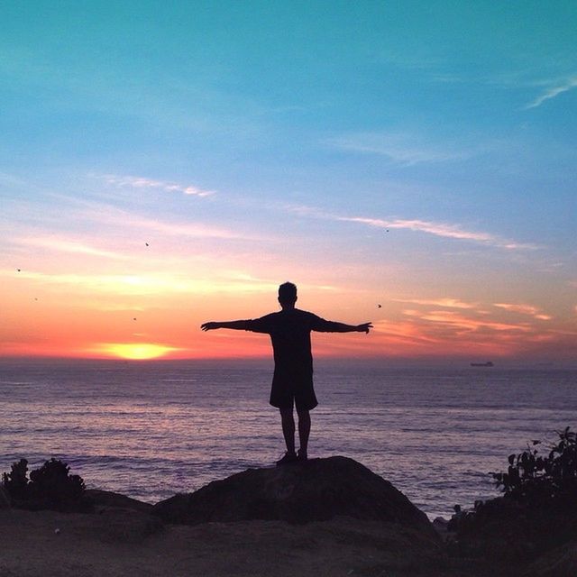 SILHOUETTE OF WOMAN STANDING ON BEACH AT SUNSET
