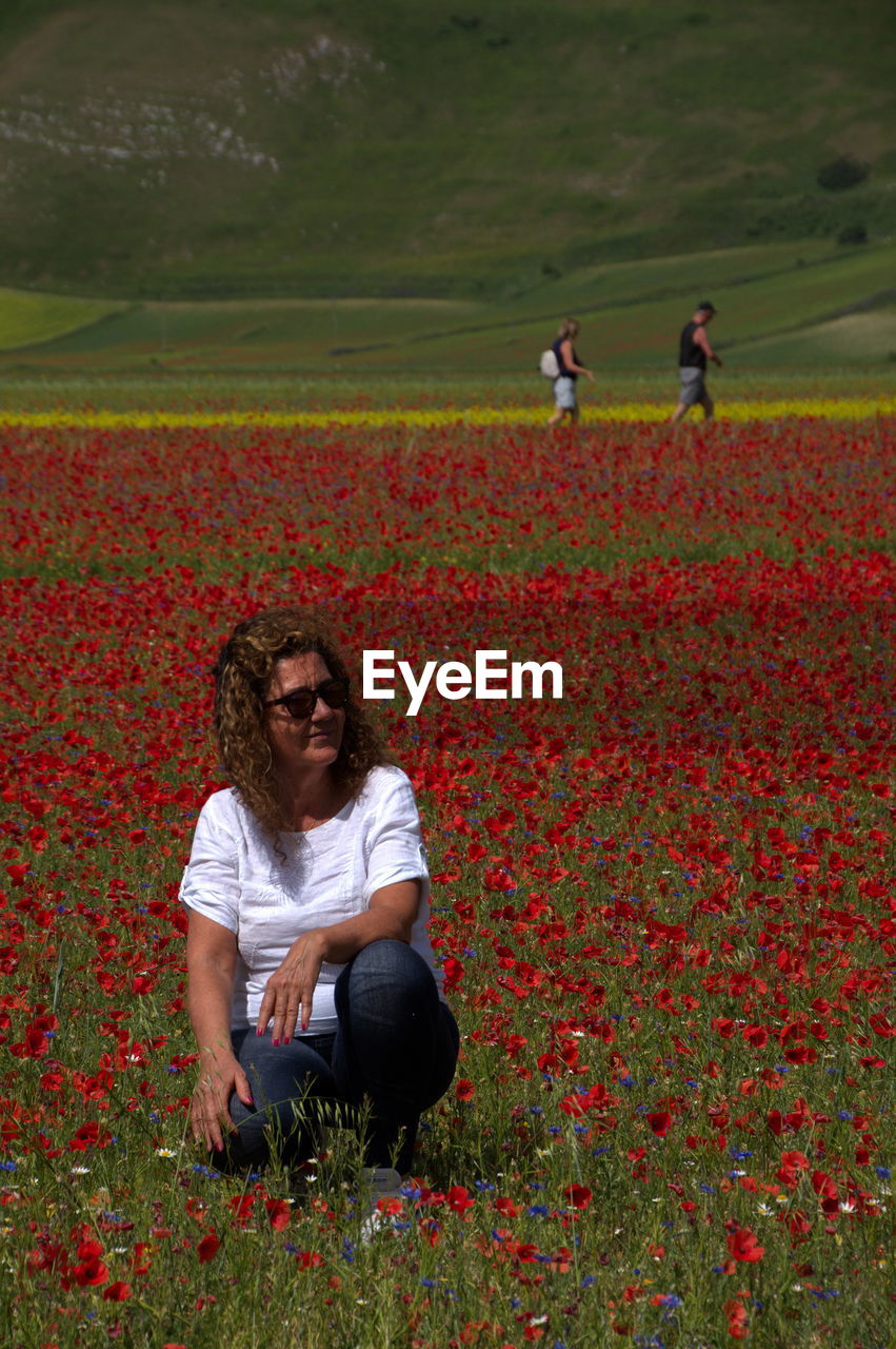 Young woman by red poppy flowers on field