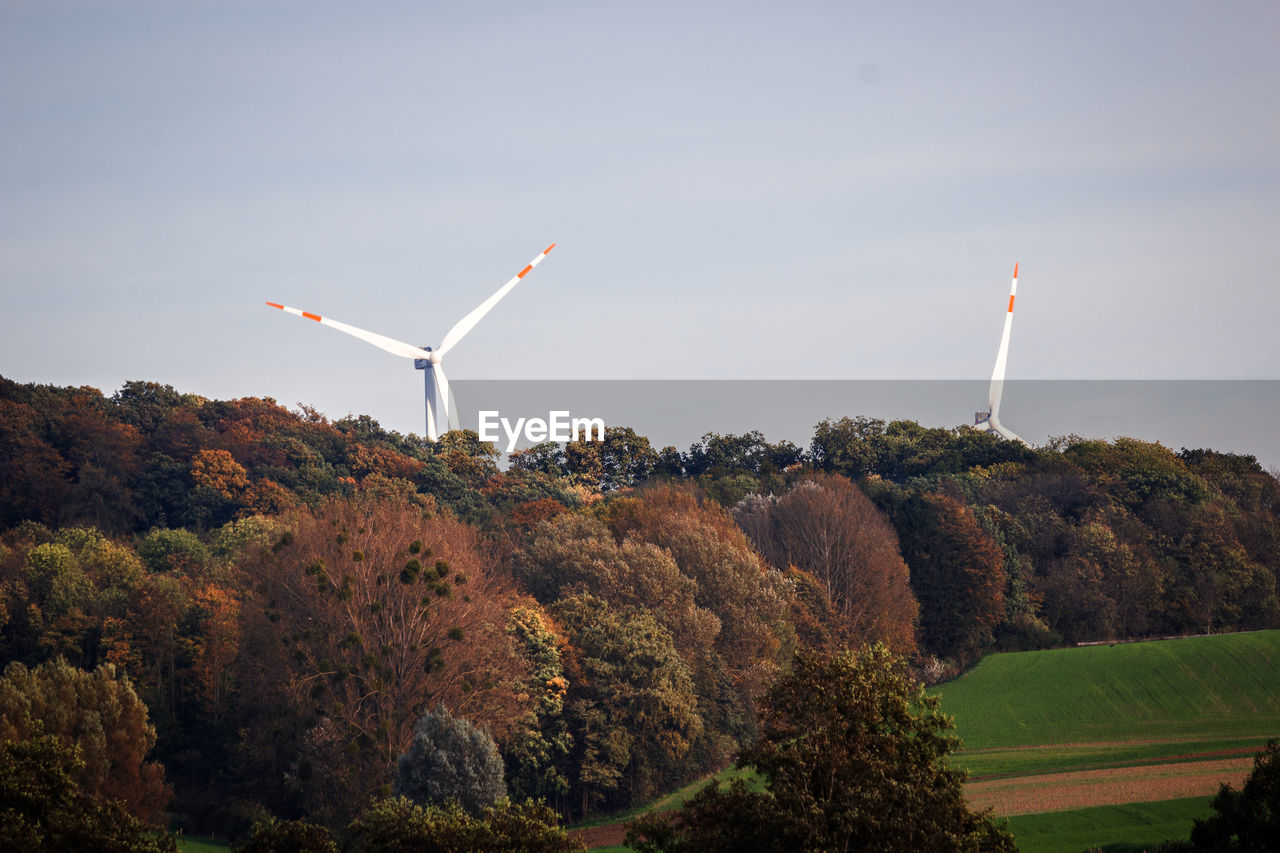 Windmills by forest against sky during autumn