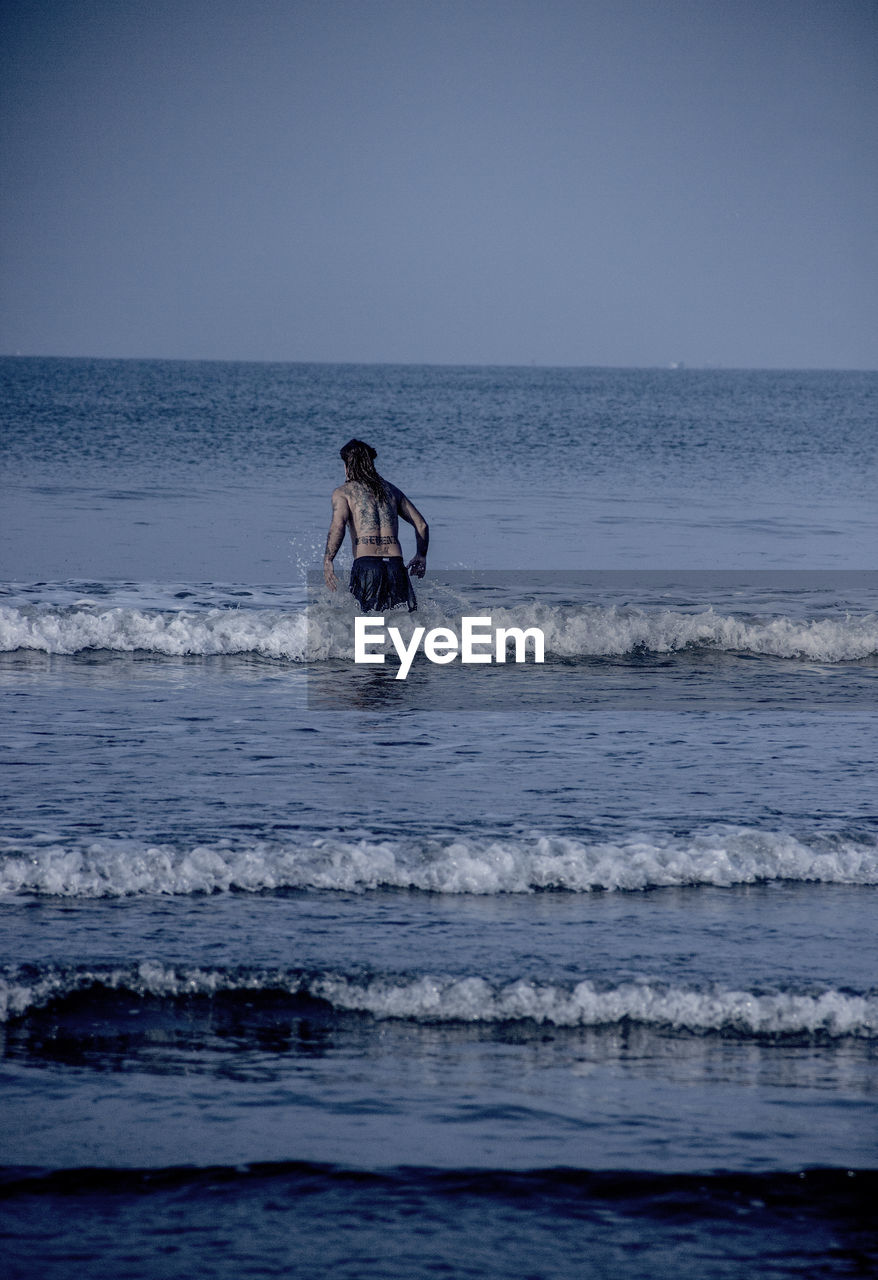 Rear view of shirtless man standing in sea against clear sky