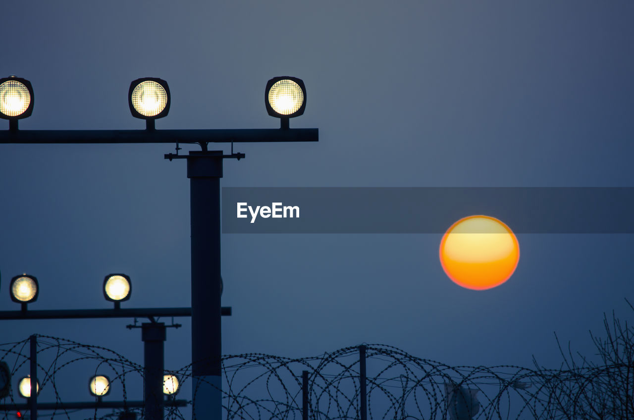 Low angle view of illuminated guiding lights against sun during sunset