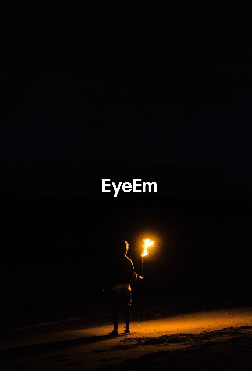 Silhouette man standing on illuminated street against sky at night