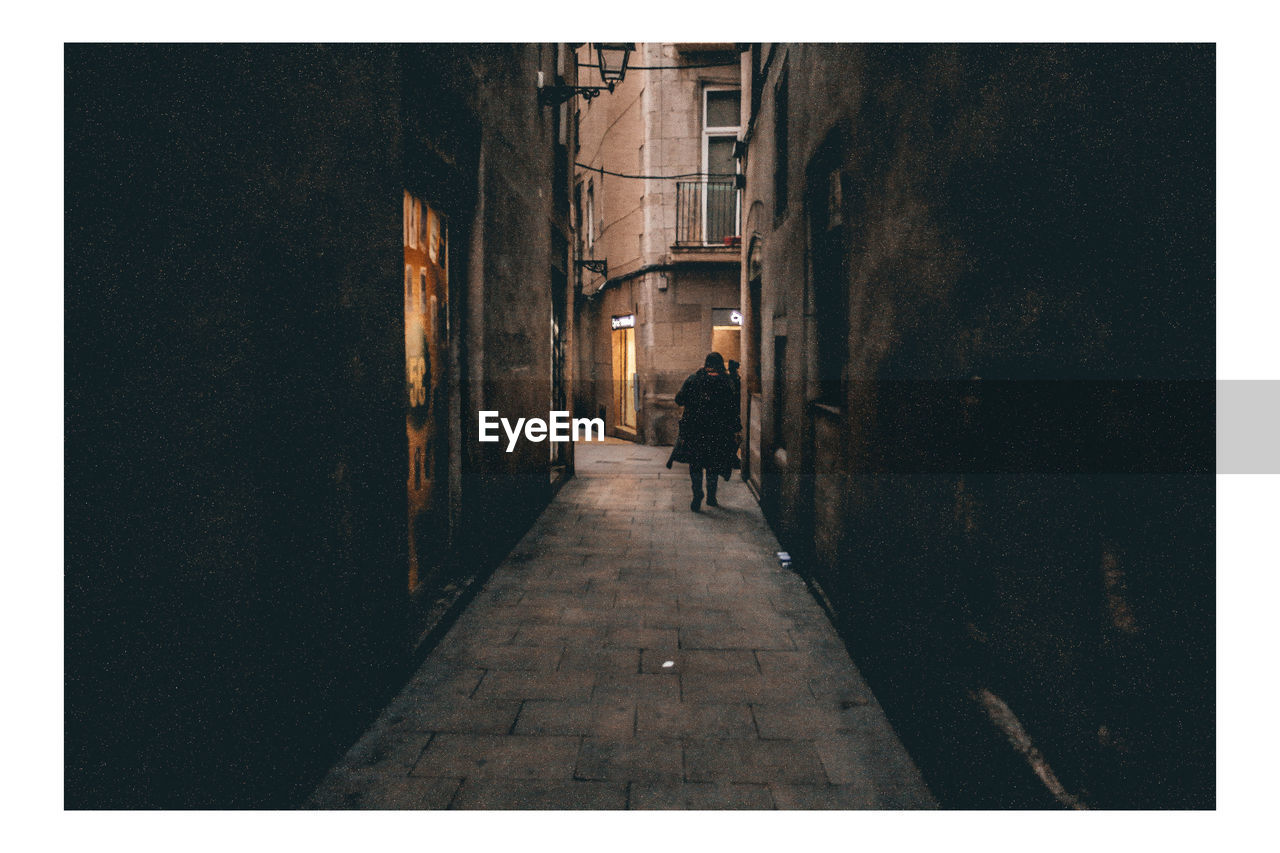 Rear view of person walking on footpath amidst buildings in city