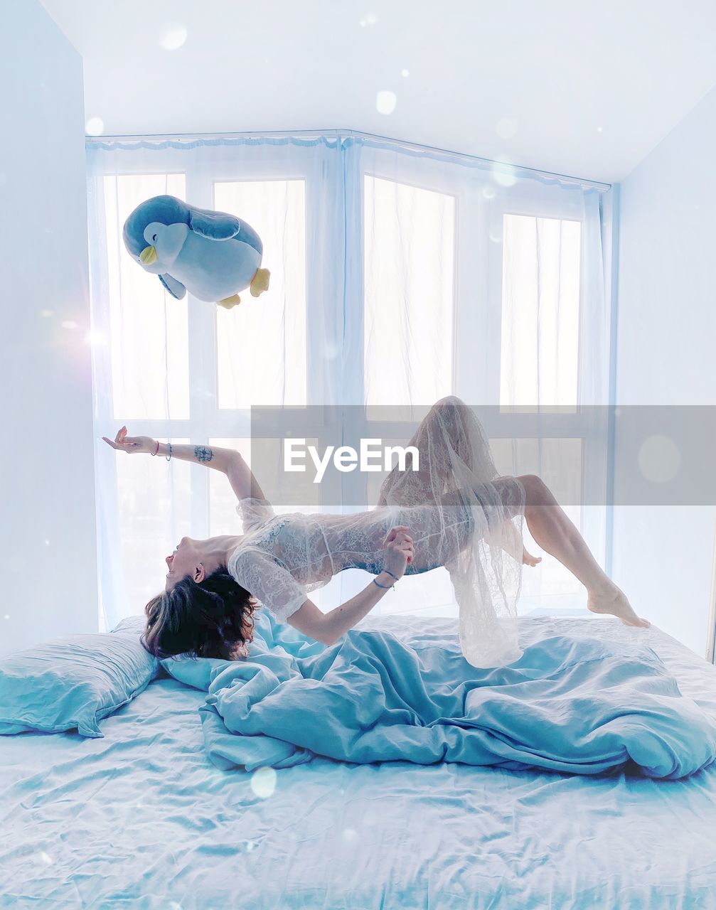 Side view of woman levitating with toy over bed at home