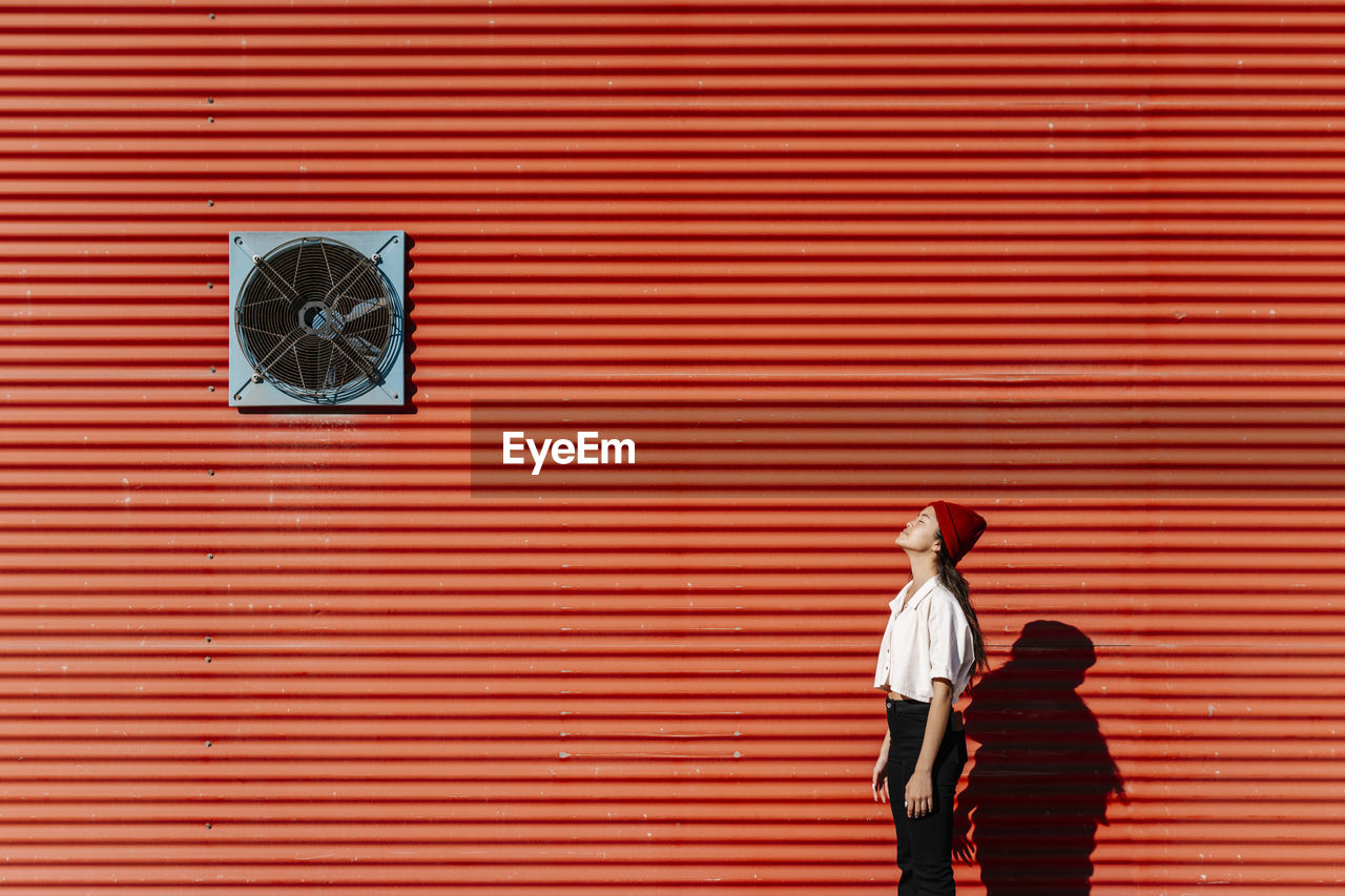 Young woman standing with eyes closed at red corrugated wall