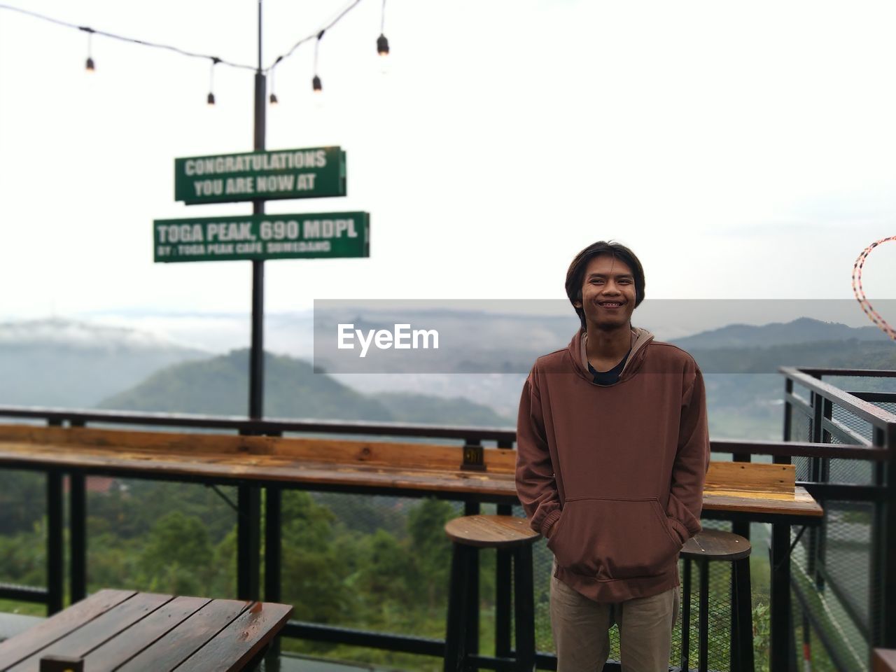 Portrait of young man standing on railing against sky