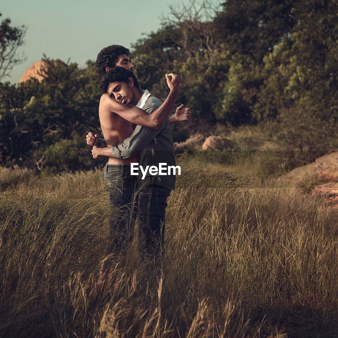 Side view of gay couple embracing on grassy field