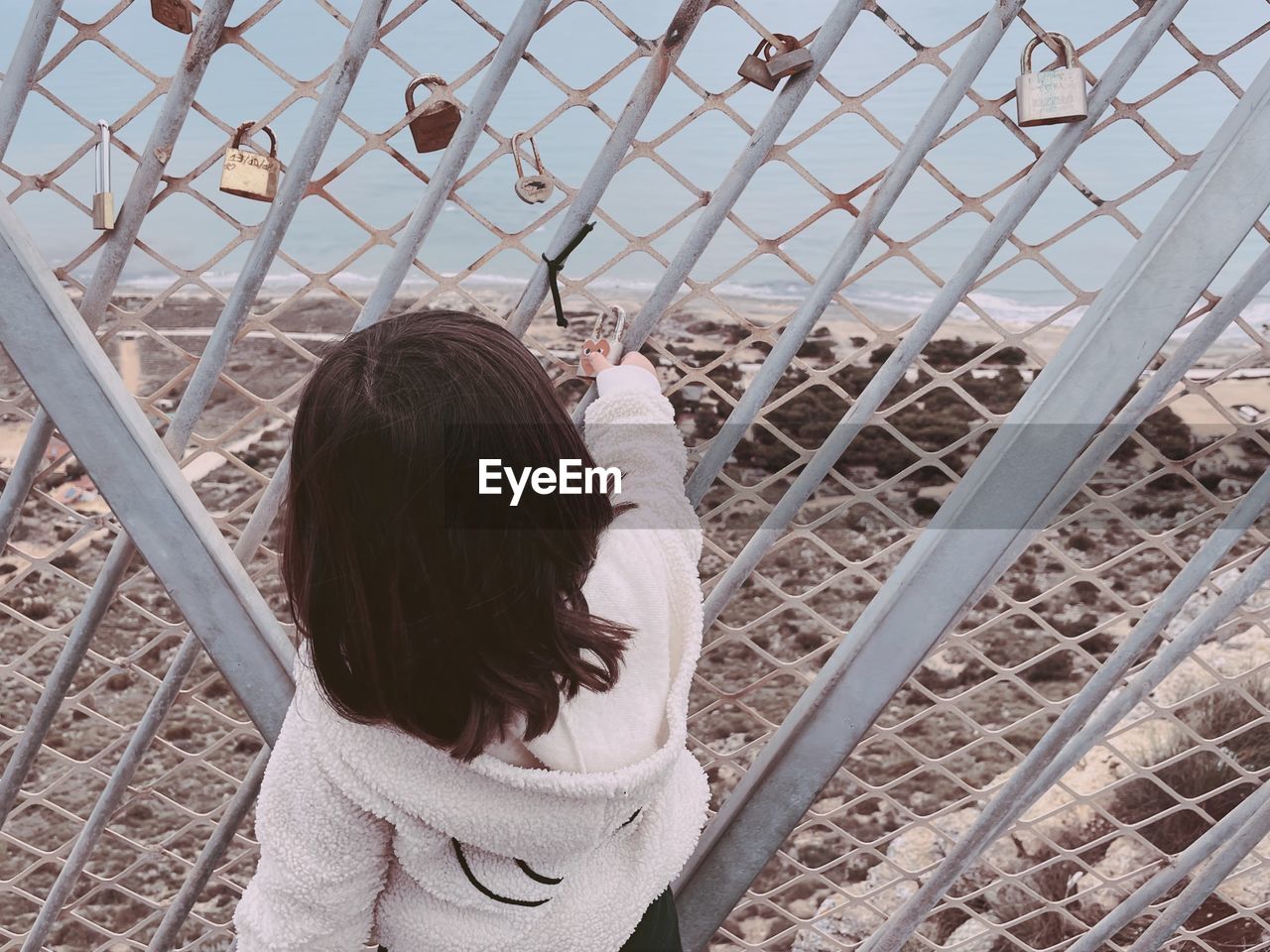 Rear view of girl holding love lock standing by chainlink fence