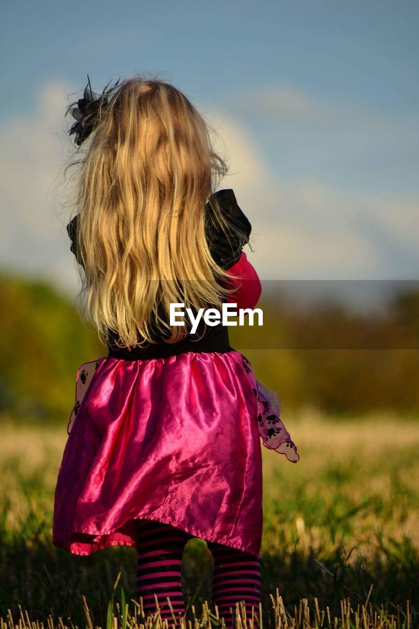 Rear view of girl standing on field against sky