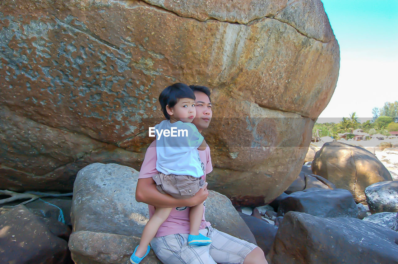 Portrait of son with father on rock at beach