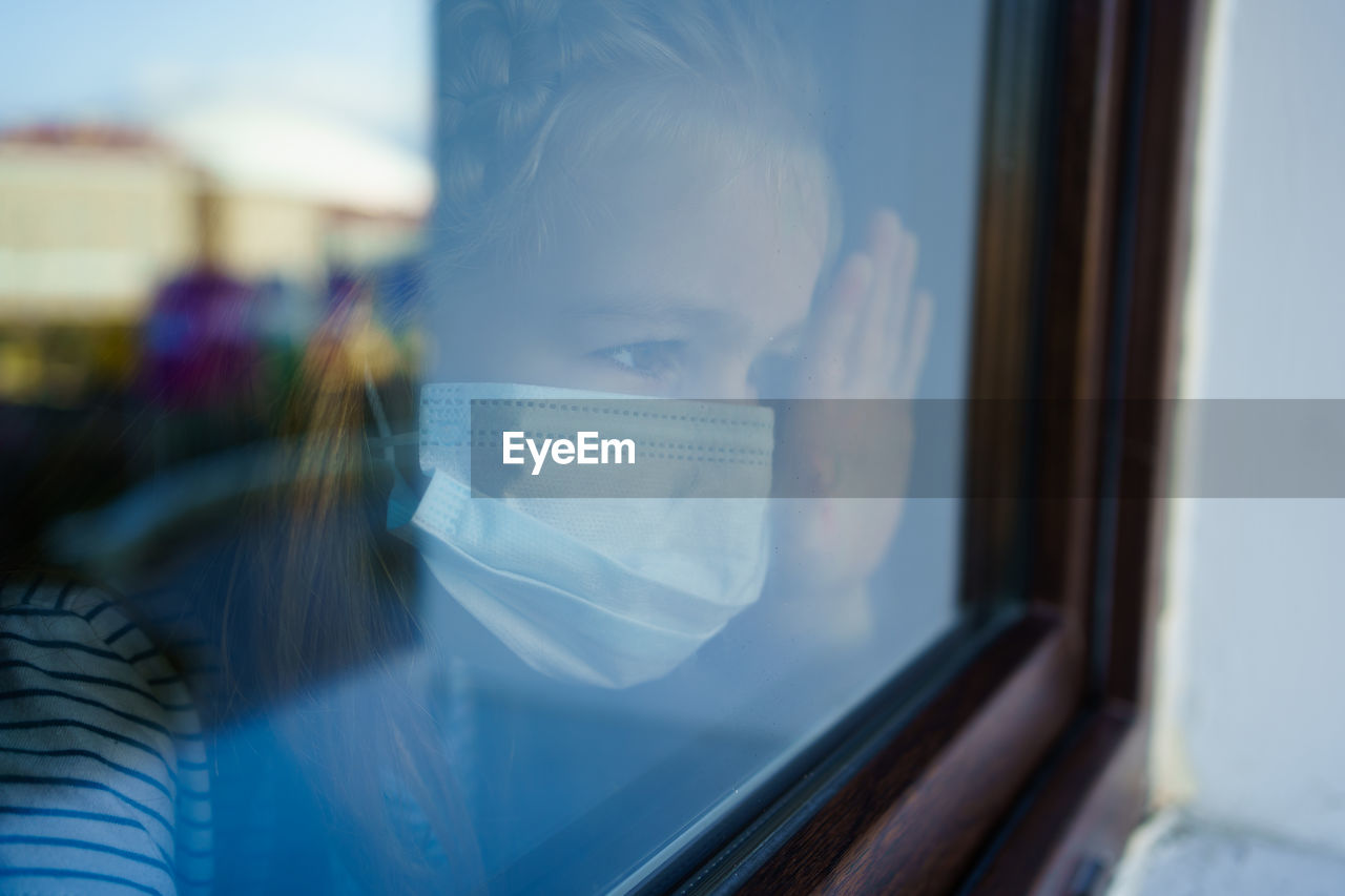 Girl wearing mask while looking away through window